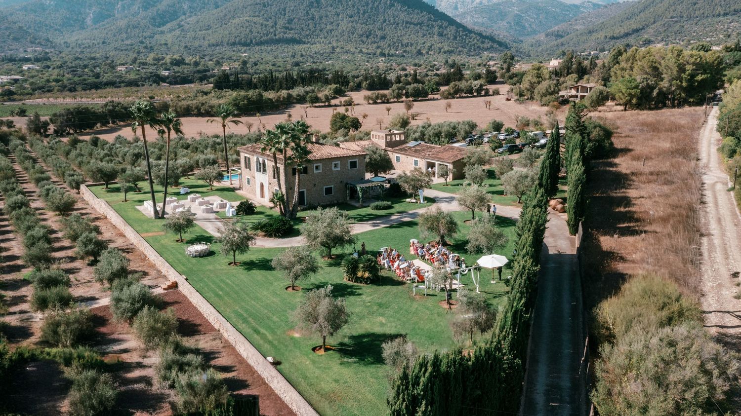 Aerial view of a rustic stone villa surrounded by olive trees and lush gardens in a scenic Mediterranean valley. Mallorca wedding photograph