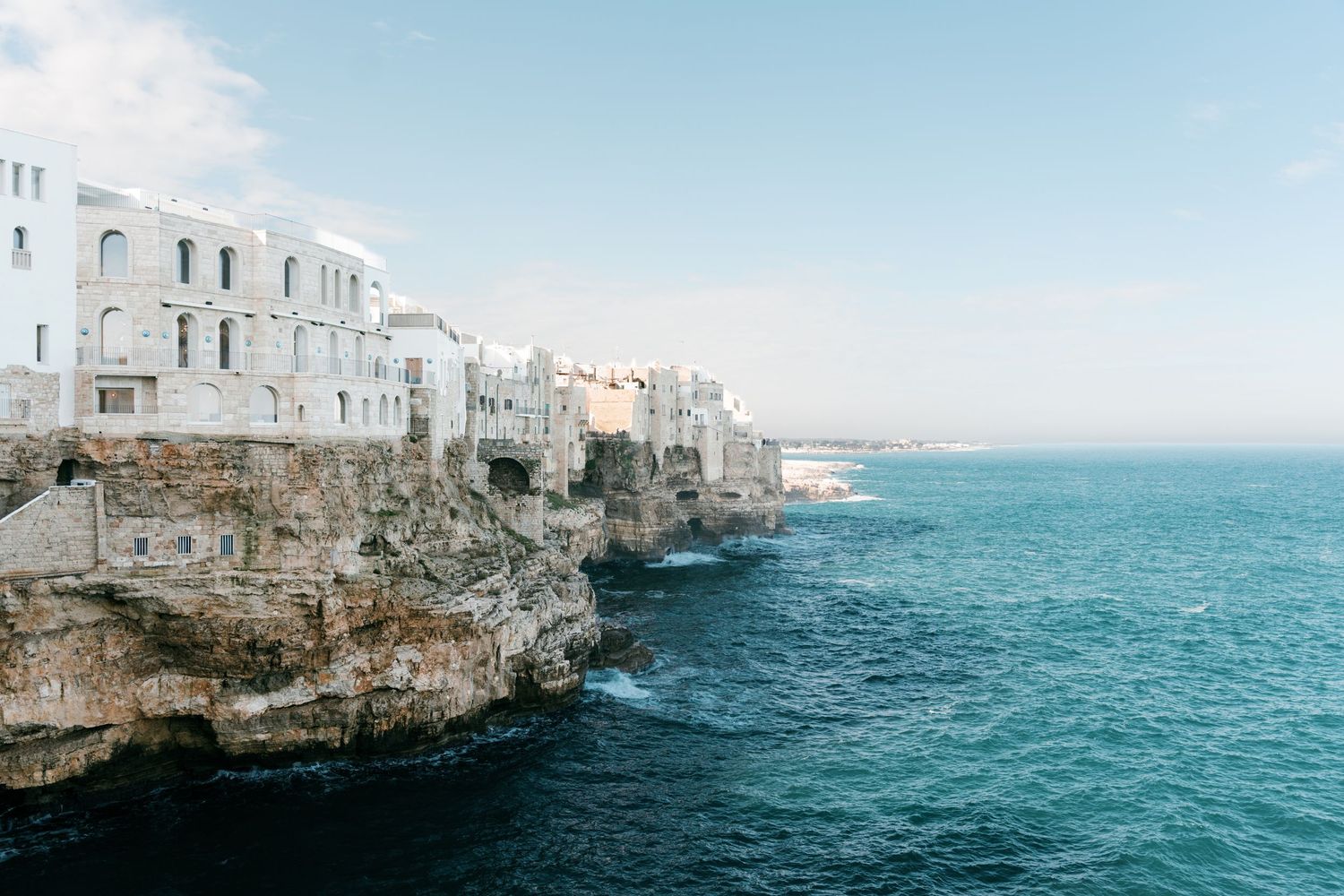 White buildings perched on dramatic cliffs overlooking the turquoise Mediterranean Sea in Polignano a Mare, Italy. Puglia wedding photograph
