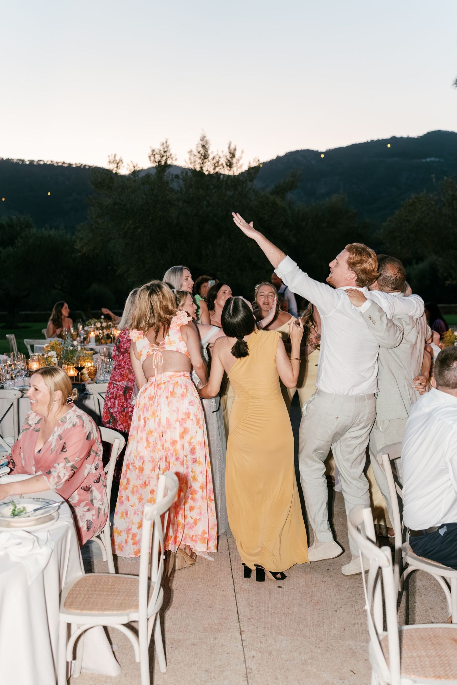 Wedding guests dance and celebrate at an outdoor evening reception surrounded by mountains. Mallorca wedding photographer, filmmaker