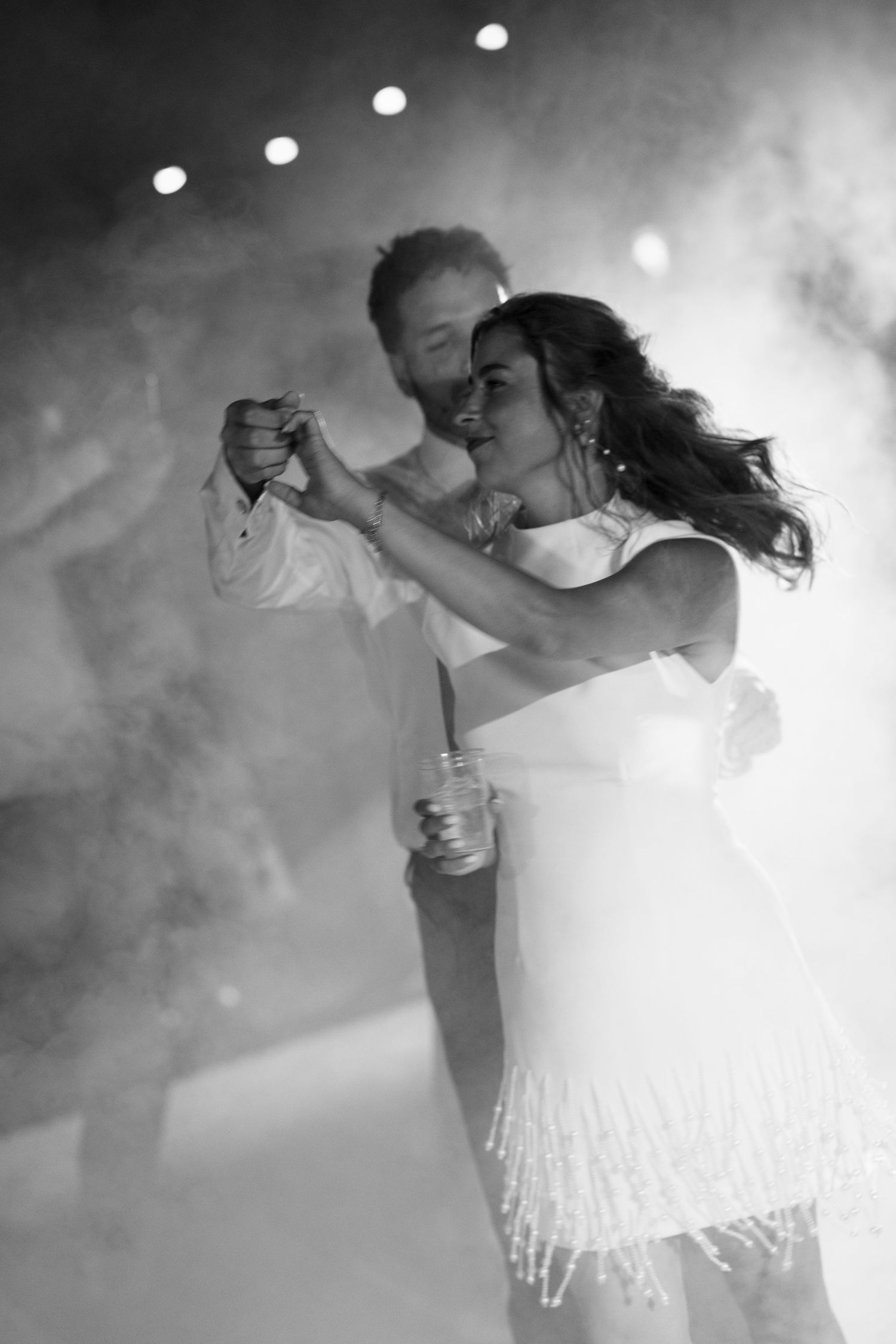 Black and white photo of a couple sharing their first dance, surrounded by atmospheric fog and soft stage lighting.