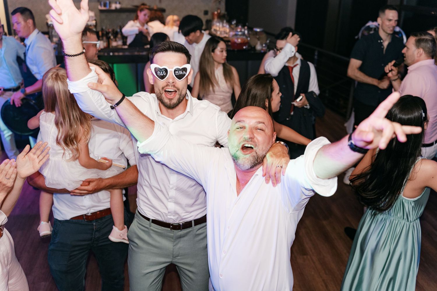 Two men with heart sunglasses dancing and celebrating energetically at wedding reception. Italy wedding photographer
