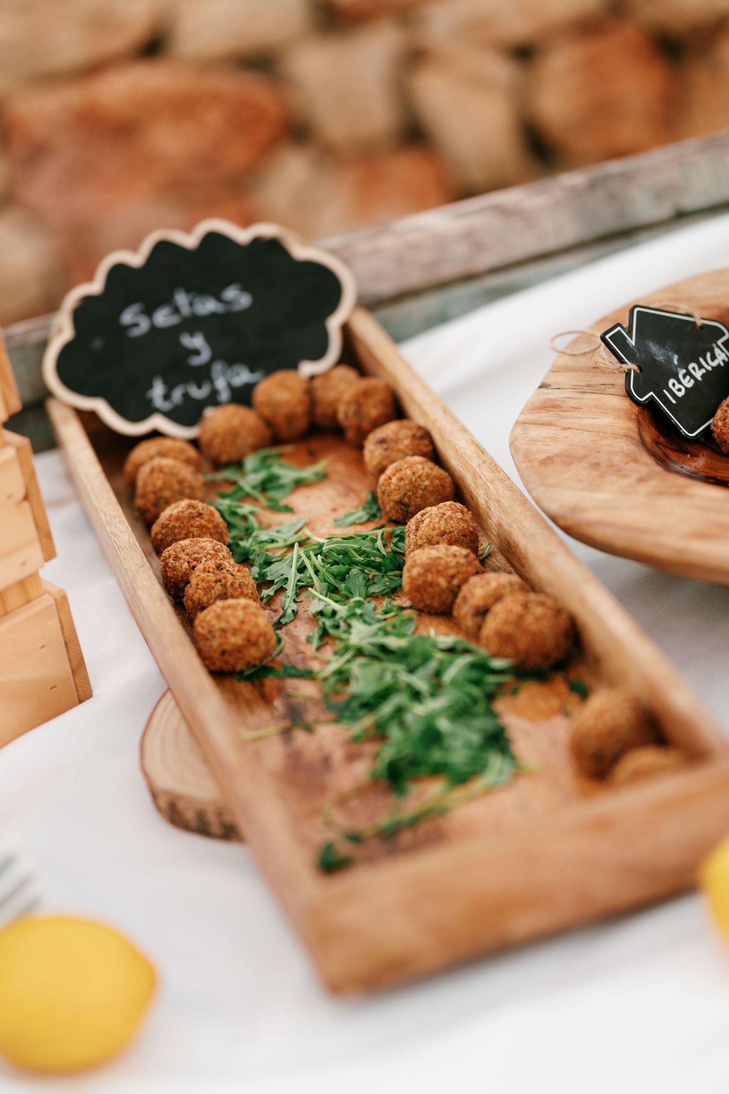 Wooden tray of golden mushroom and truffle croquettes with fresh herbs beside a chalkboard sign at a rustic buffet.