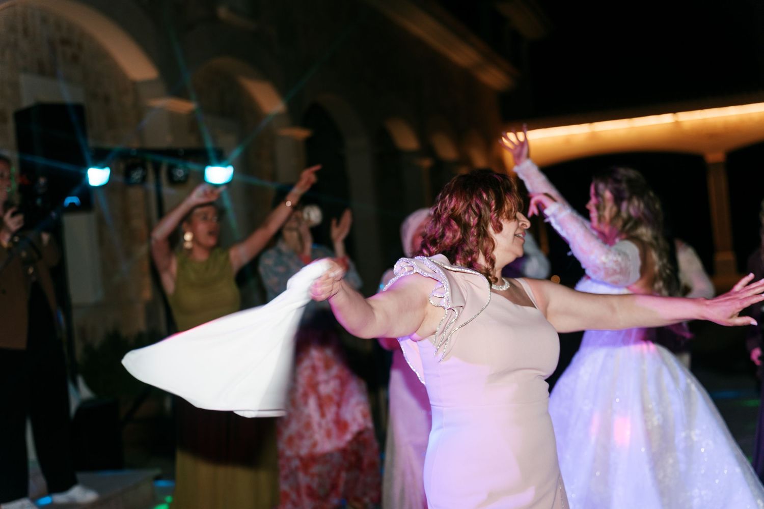 Bride and guests dancing joyfully at a wedding reception, with colorful lights illuminating the festive celebration in Mallorca.