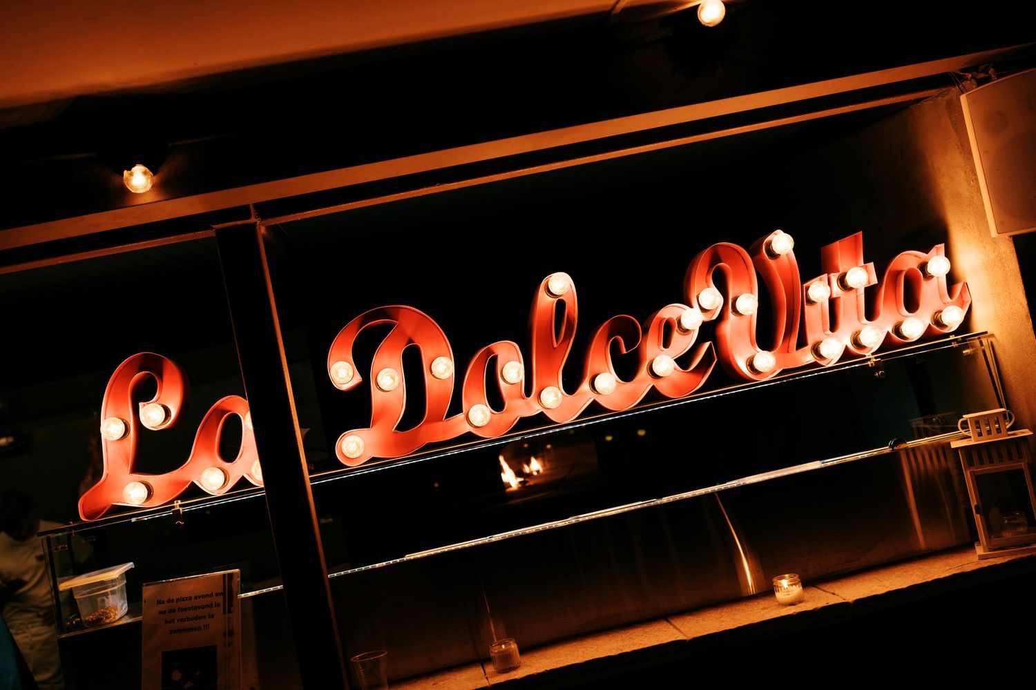 Illuminated red neon sign reading La Dolce Vita on a dark restaurant facade at night.