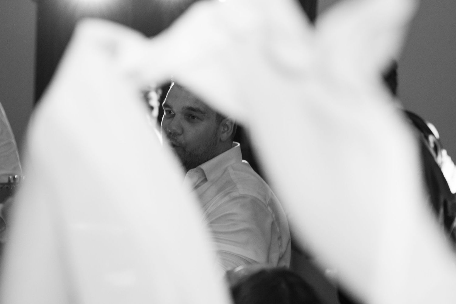 Candid black and white portrait of wedding guest surrounded by blurred white fabric foreground. Tuscany wedding photographer, filmmaker