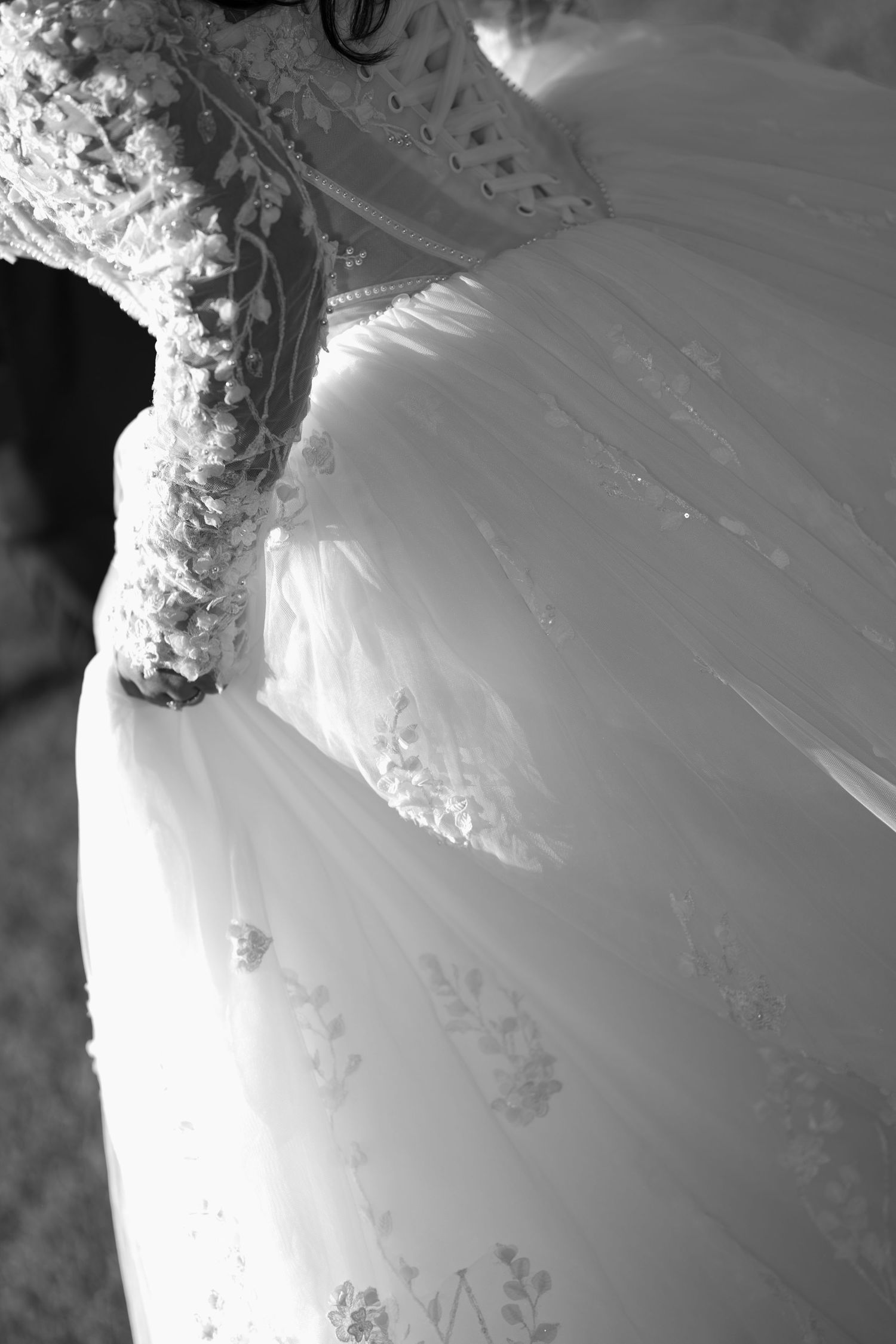 Black and white photo of a bride in a lace wedding gown with embroidered sleeves and a flowing tulle skirt.