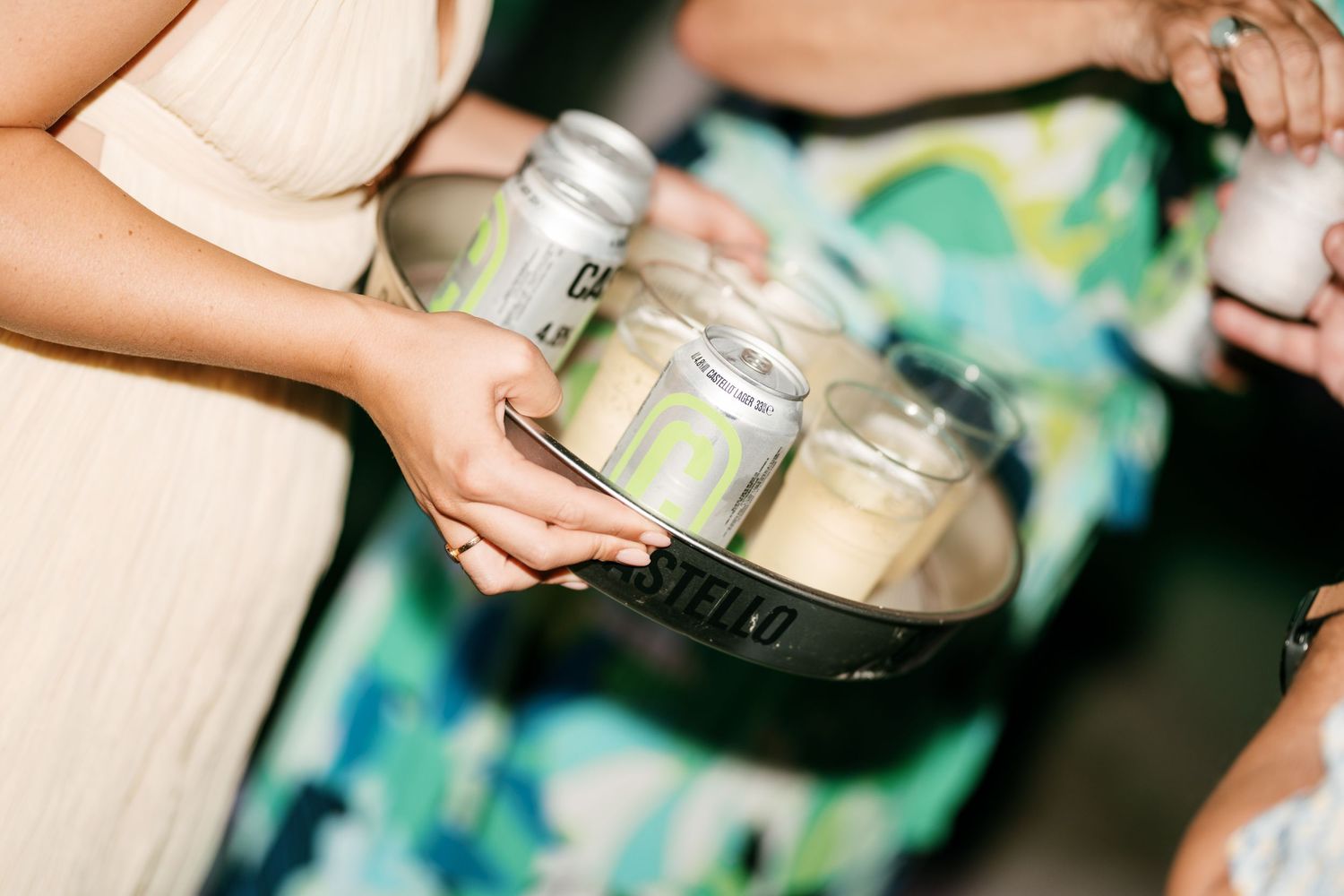 Server holds tray of Stella Artois beer cans with glasses at elegant wedding reception.