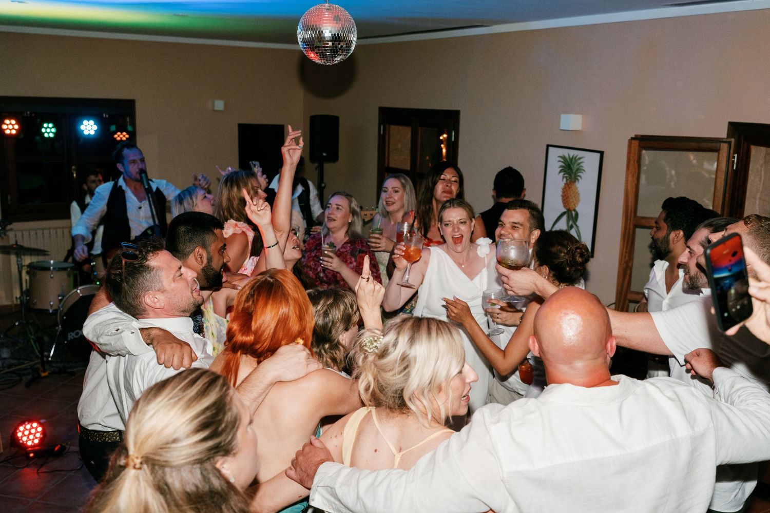 Colorful photo of wedding guests packed on dance floor under disco ball at lively reception. Puglia wedding photographer,