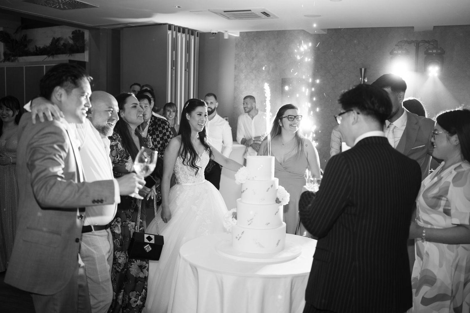 Black and white photo of wedding guests gathered around the couple near their cake. Italy wedding photographer and filmmaker
