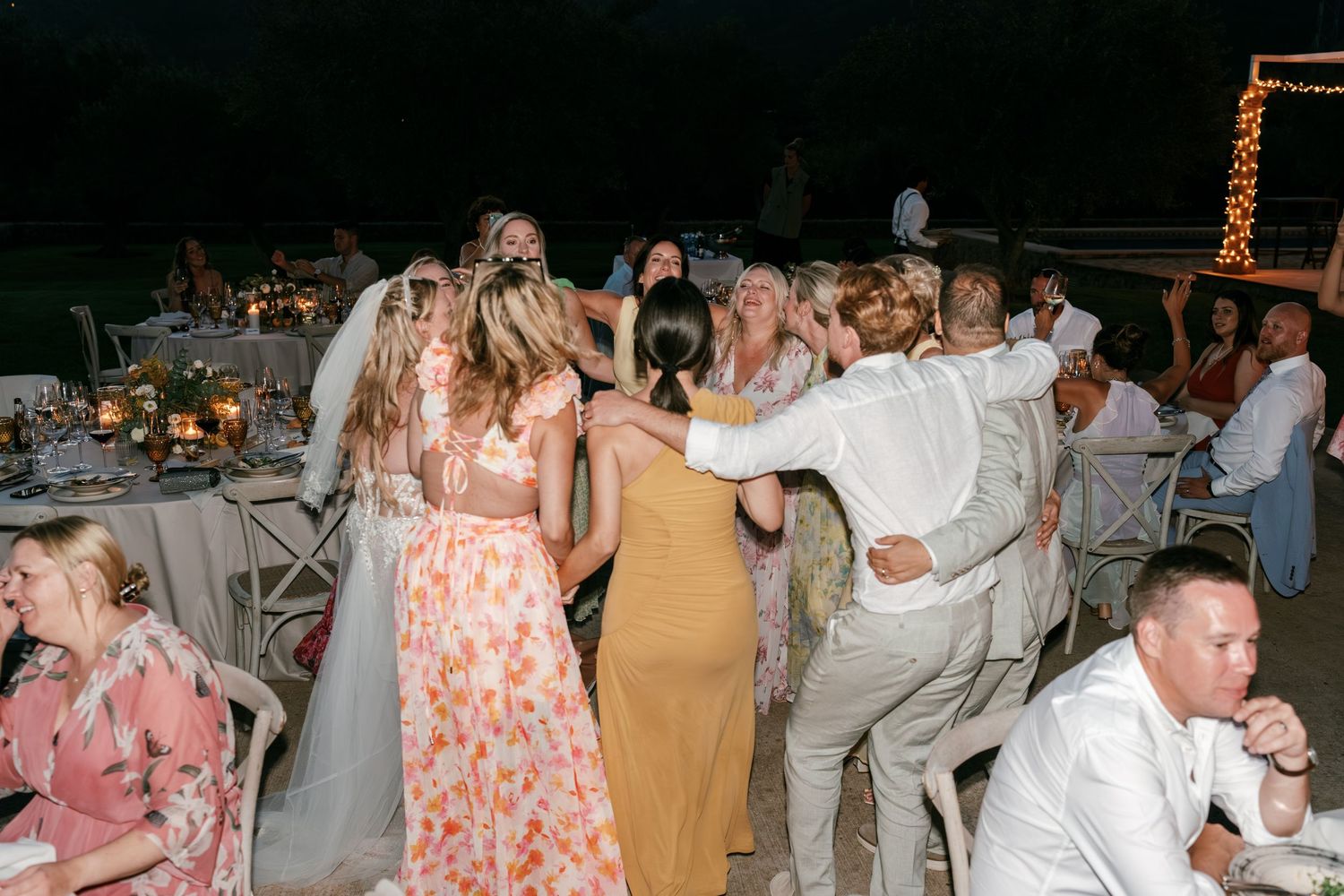 Bride and wedding guests dance together joyfully at an outdoor evening reception celebration. Tuscany wedding photographer, filmmaker