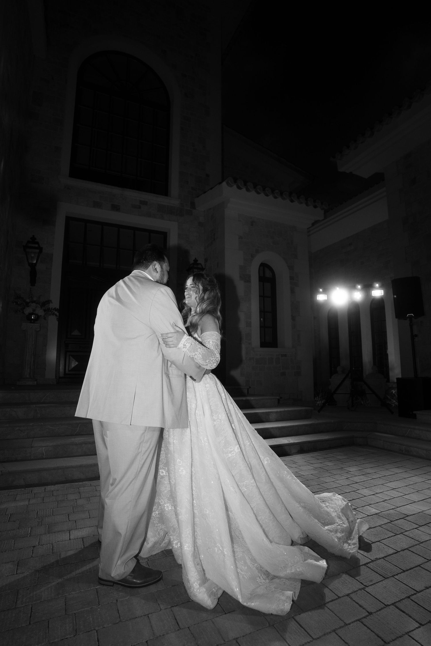 Black and white photo of a bride and groom sharing a romantic dance outside a historic building at night in Mallorca.