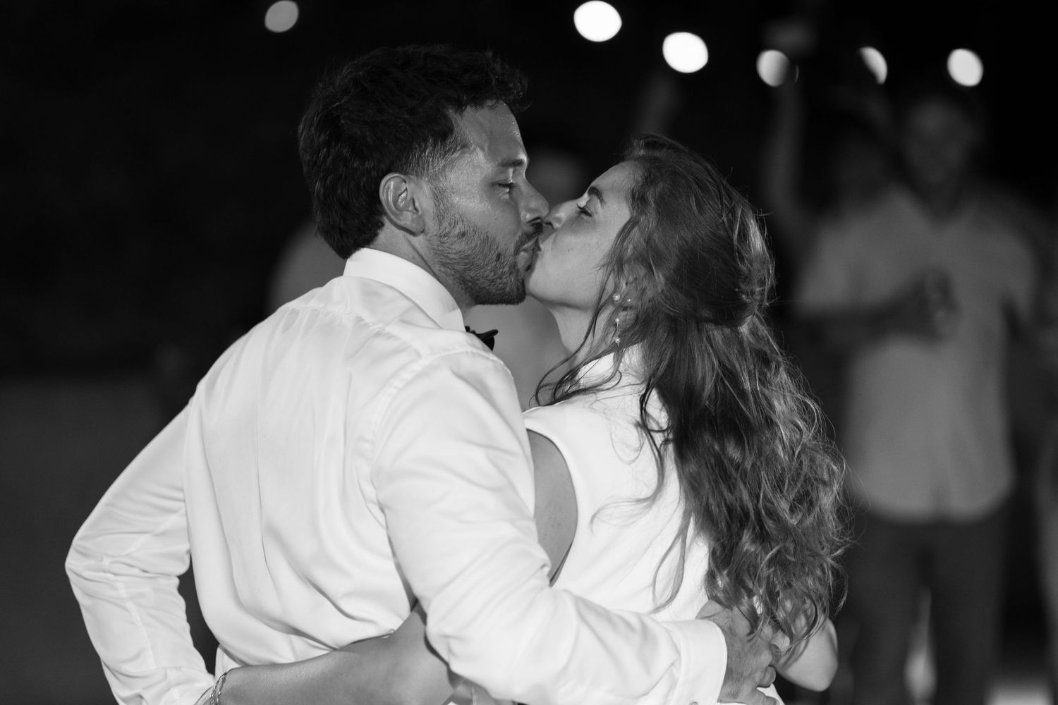 Black and white photo of a couple sharing a passionate kiss during their outdoor wedding reception.