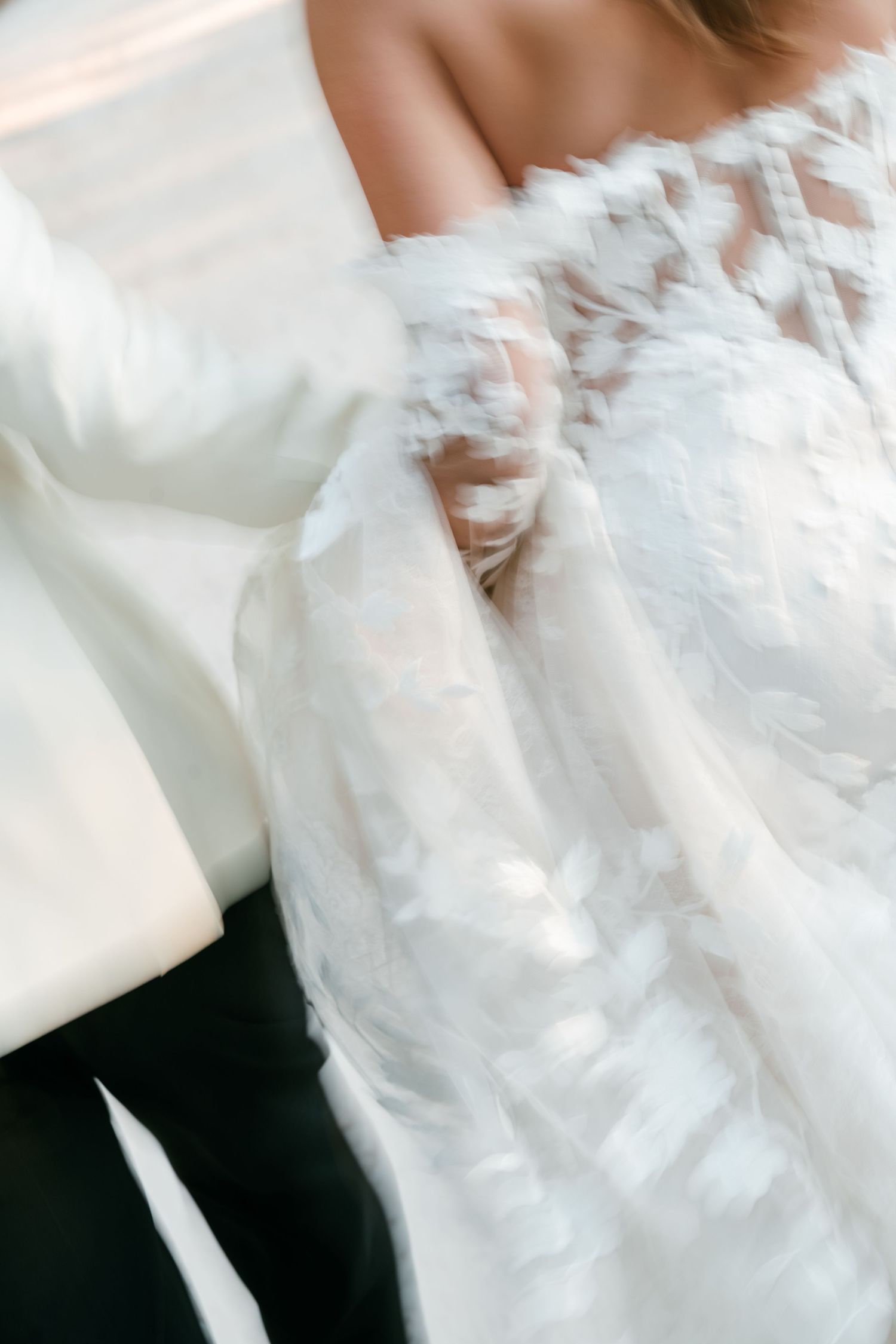 Blurred motion shot of a bride in a white lace long-sleeve wedding dress holding hands with a groom in a white suit.
