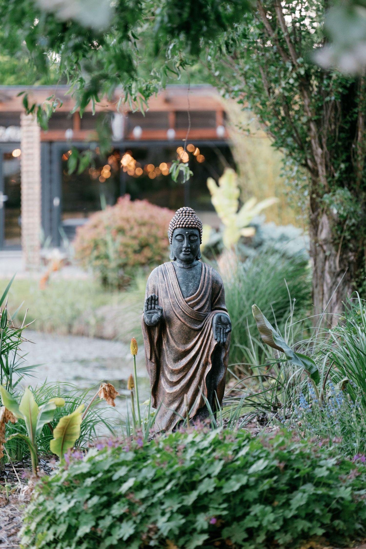 Bronze Buddha statue standing peacefully among lush garden greenery and plants. Mallorca wedding photographer and filmmaker.