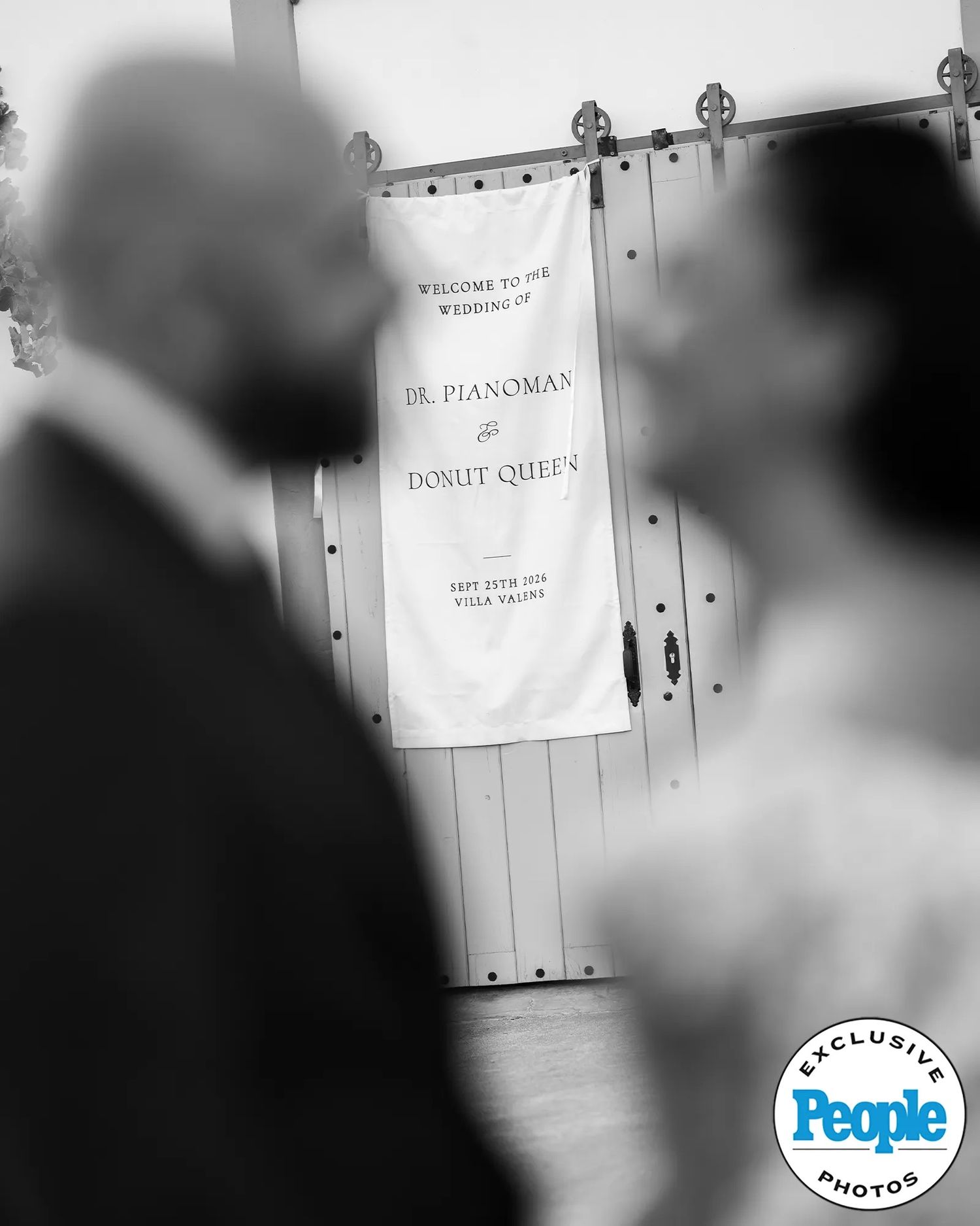 Blurred silhouettes of a couple in the foreground face a hanging banner welcoming guests to the wedding of Dr. Pianoman and Donut Queer.