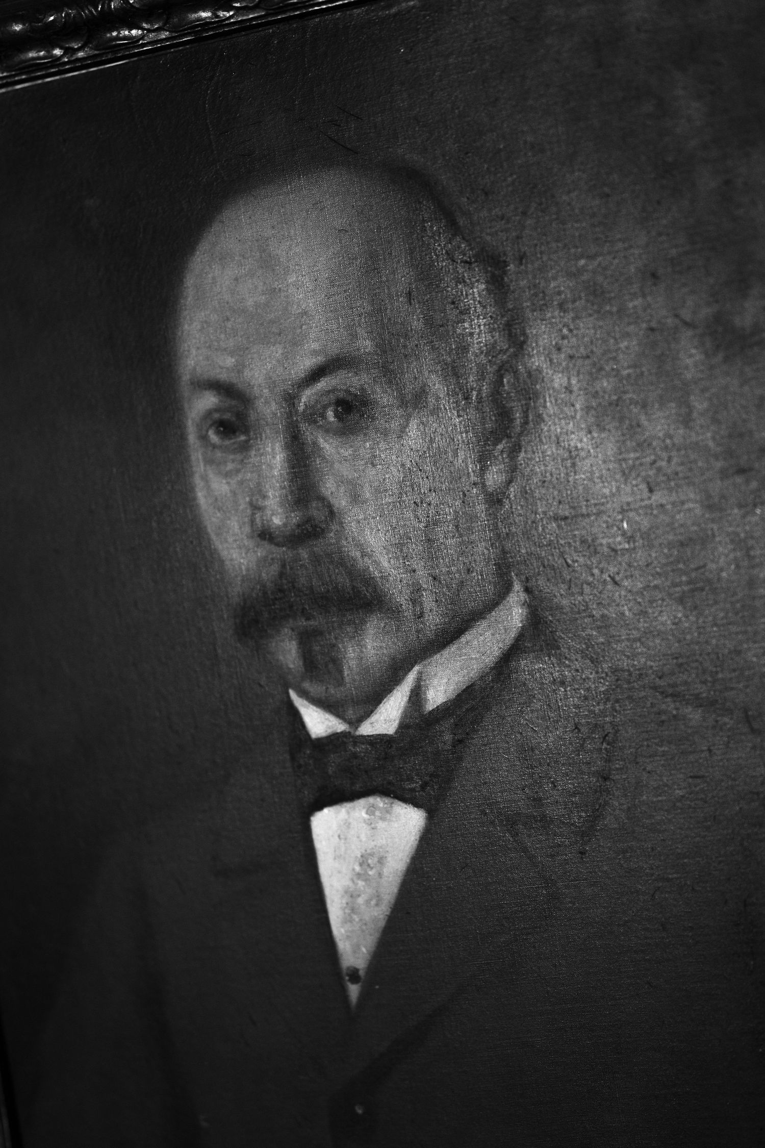 Black and white vintage portrait painting of a bald man with a mustache and goatee wearing a dark suit and bow tie.