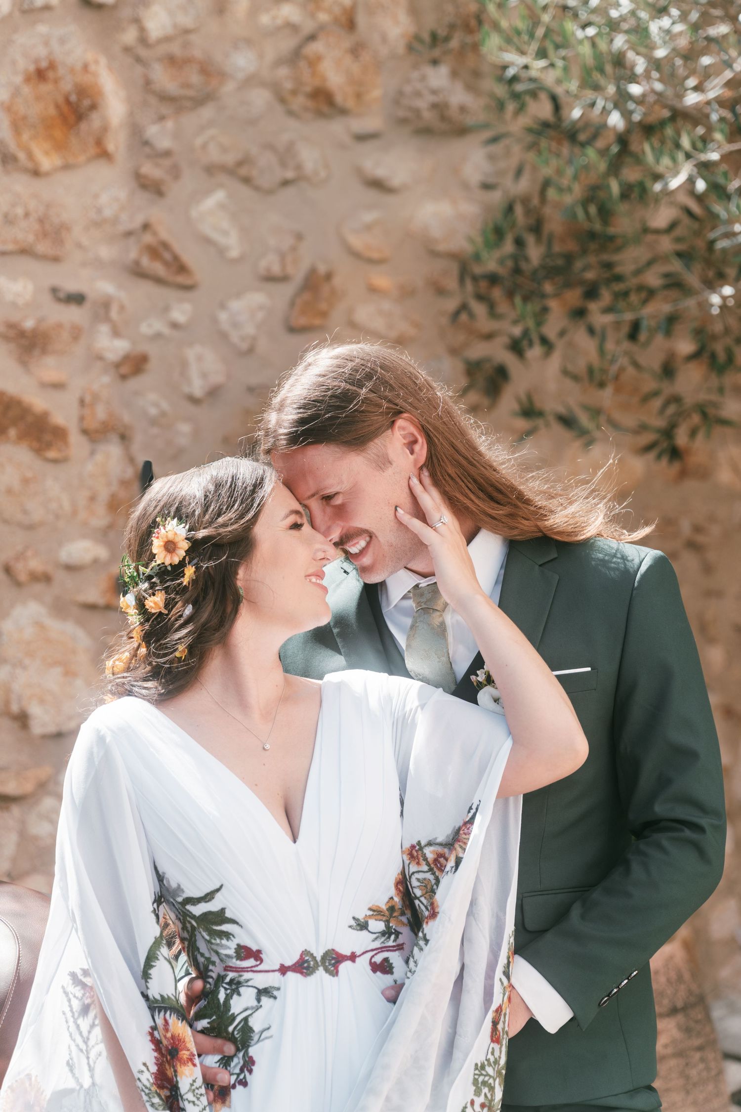 Bride and groom smiling and touching foreheads against a rustic stone wall backdrop. Tuscany wedding photographer, filmmaker