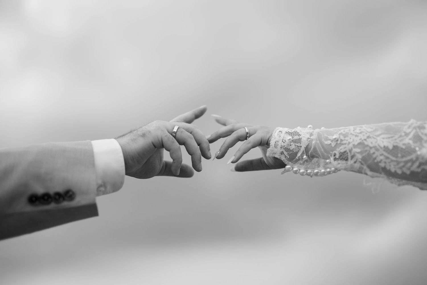 Black and white wedding photo of bride and groom gently touching fingertips, bride wearing lace sleeve and ring in Mallorca.