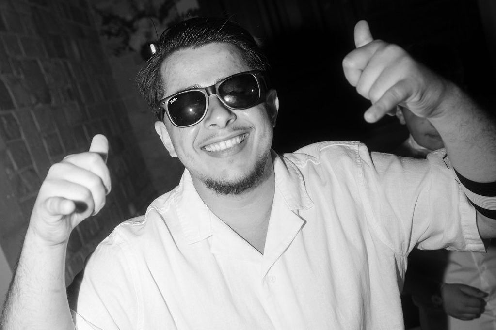 Young man in sunglasses giving thumbs up, smiling in black and white photo wearing white shirt in Mallorca.
