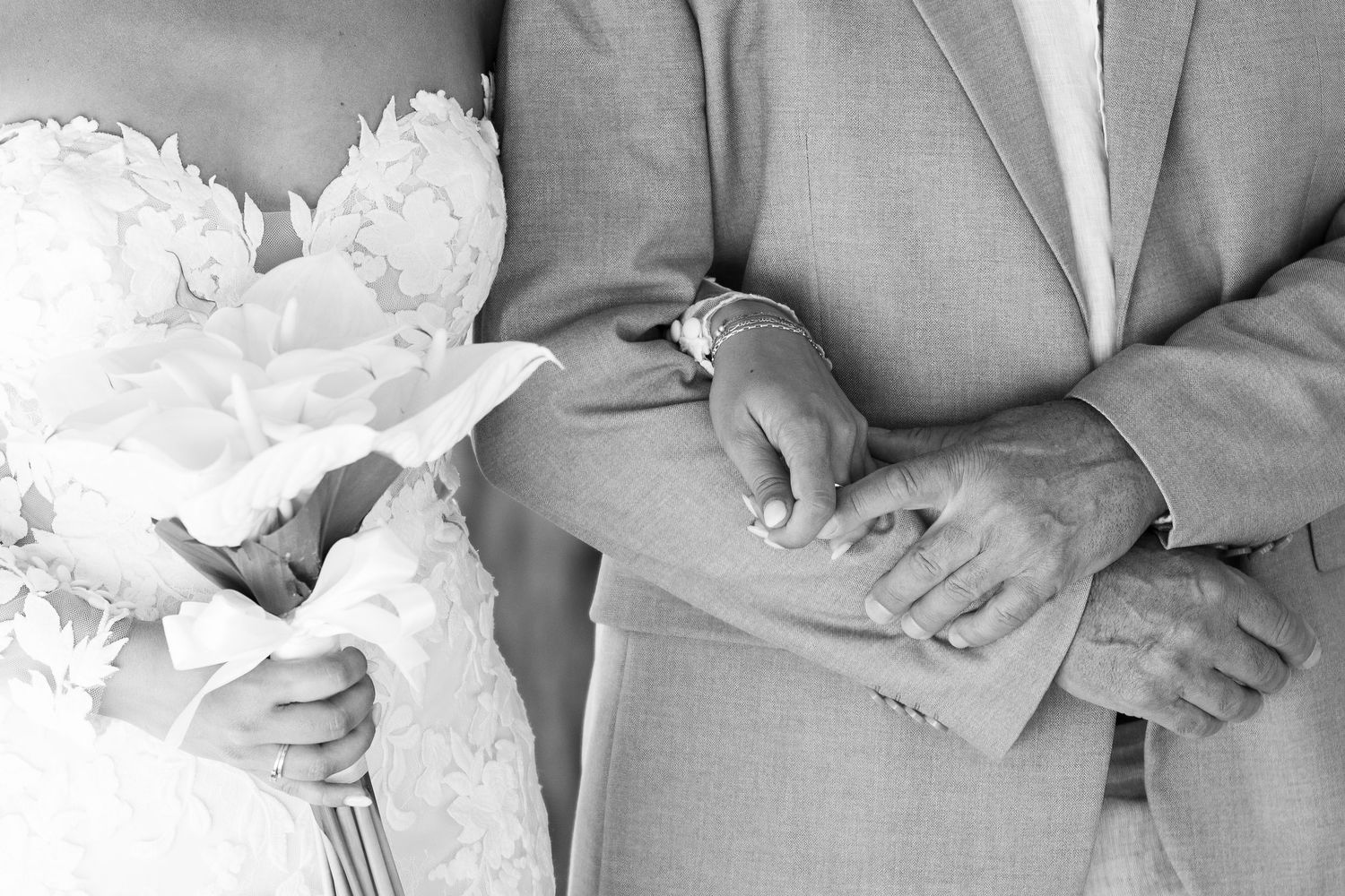 Black and white wedding photo of bride holding bouquet and groom in gray suit, hands clasped together.