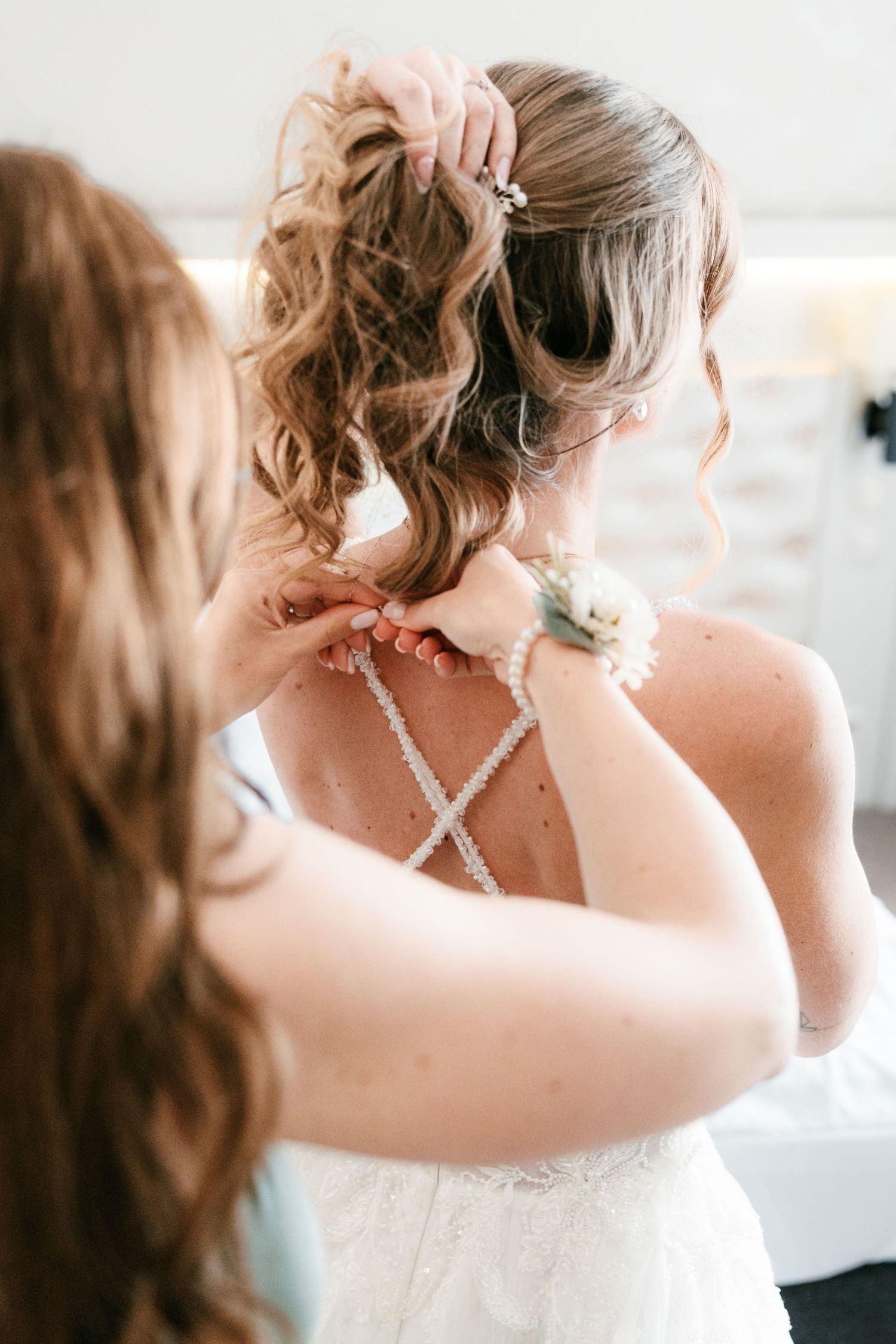 Bridesmaid fastens pearl cross-back straps on bride's lace wedding dress. Mallorca wedding photographer and filmmaker.