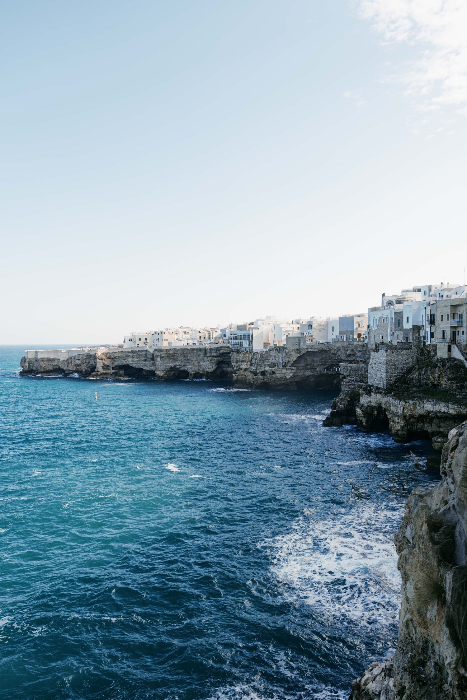White buildings perched on dramatic rocky cliffs overlooking the turquoise Adriatic Sea in Polignano a Mare, Italy. Mallorca wedding photogr