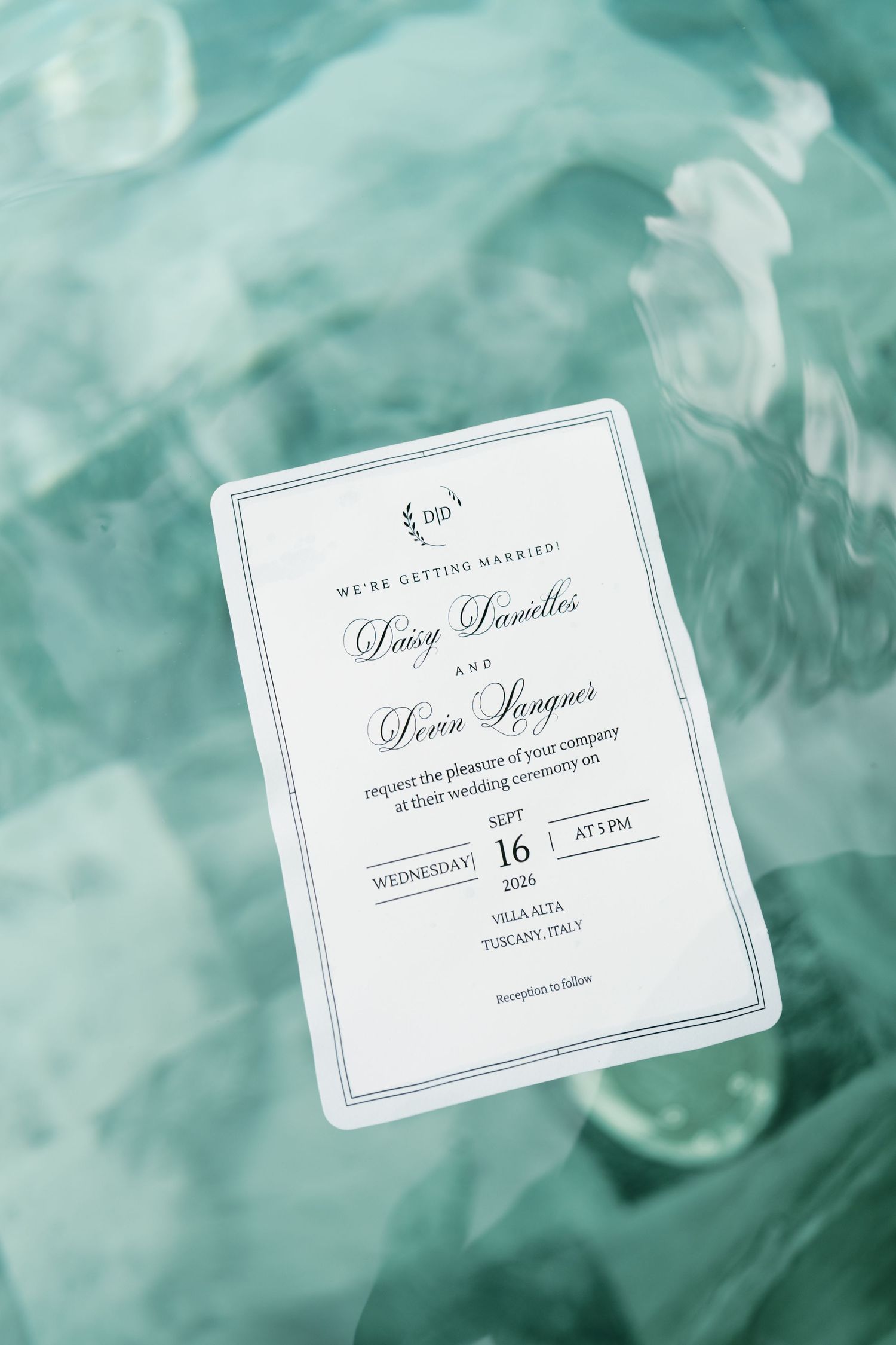 Wedding invitation for Daisy Danielles and Devin Sanger, September 16 at Villa Alta, Tuscany, Italy, resting on teal glass.