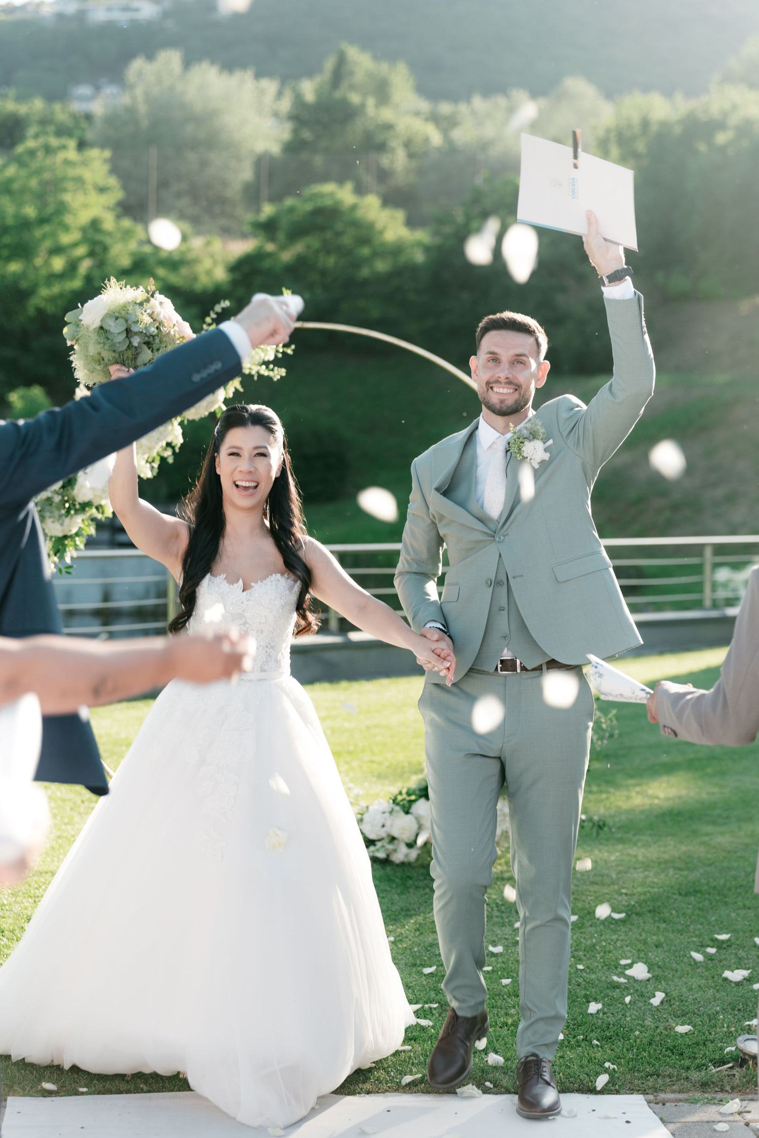 Joyful newlyweds celebrate after outdoor wedding ceremony with petals flying and guests cheering. Italy wedding photographer and filmmaker