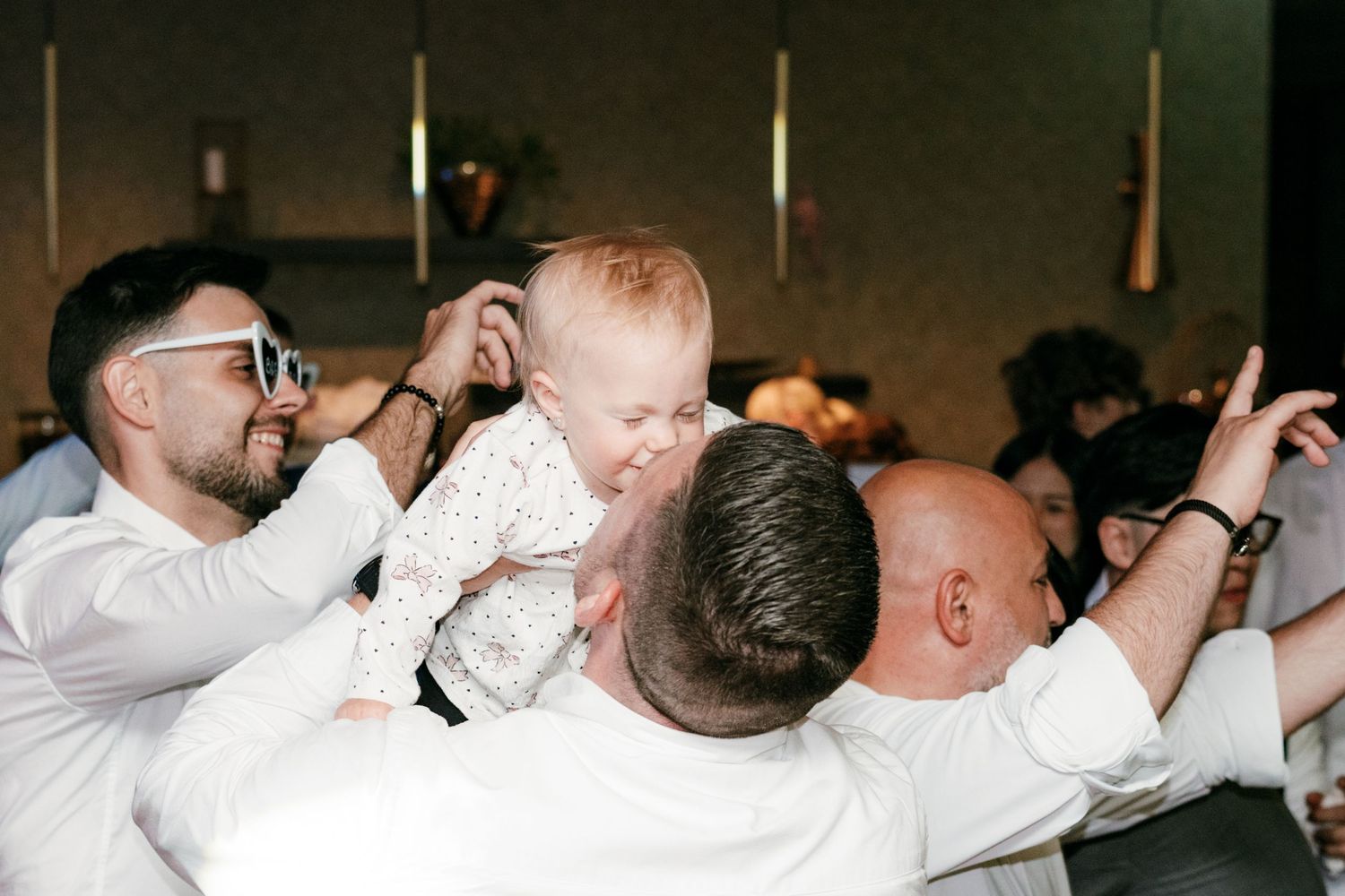 Baby being lifted joyfully above crowd at lively wedding reception celebration. Italy wedding photographer