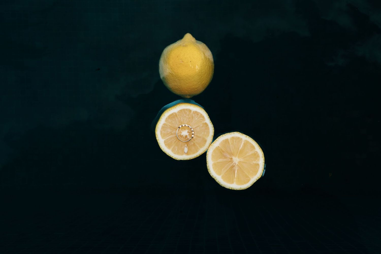 Mallorca wedding photographer. Fresh lemon cut in half beside a whole lemon on a dark background, showcasing engagement ring.