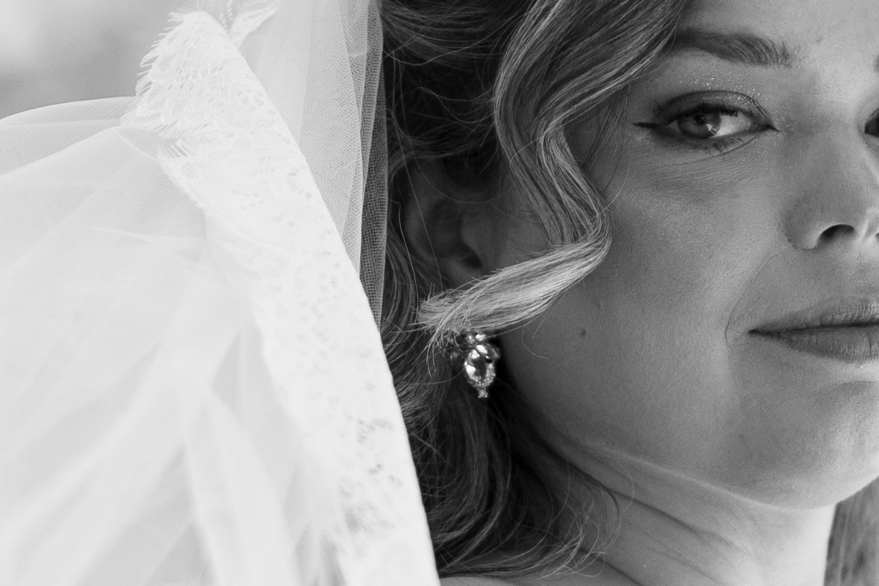 Black and white bridal portrait of a woman in a veil and earring, soft focus close-up wedding photography.