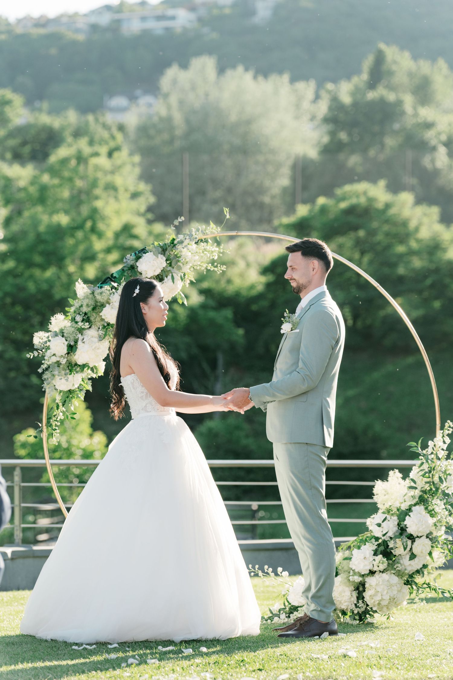 Bride and groom holding hands at a circular floral arch during an outdoor wedding ceremony. Italy wedding photographer and filmmaker