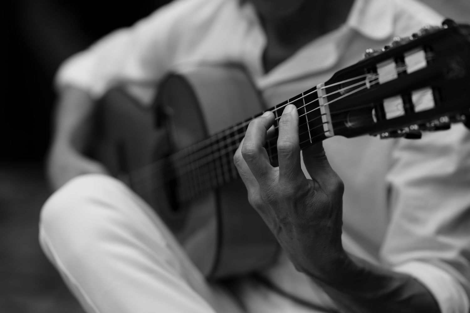 Black and white close-up of a musician's hands playing a classical guitar during a live performance.