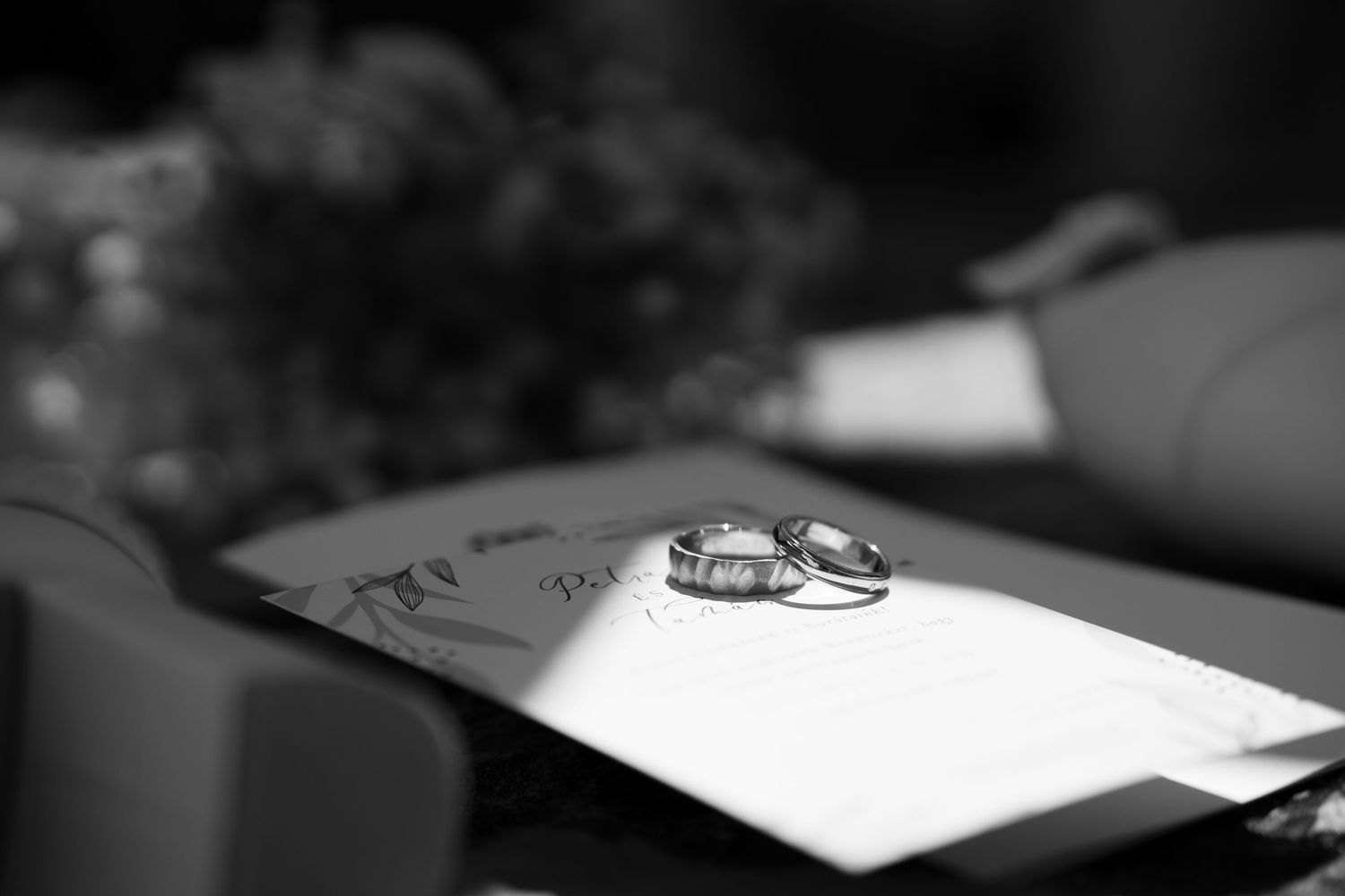 Close-up black and white photo of two wedding bands resting on a wedding program. Mallorca wedding photographer and filmmaker.