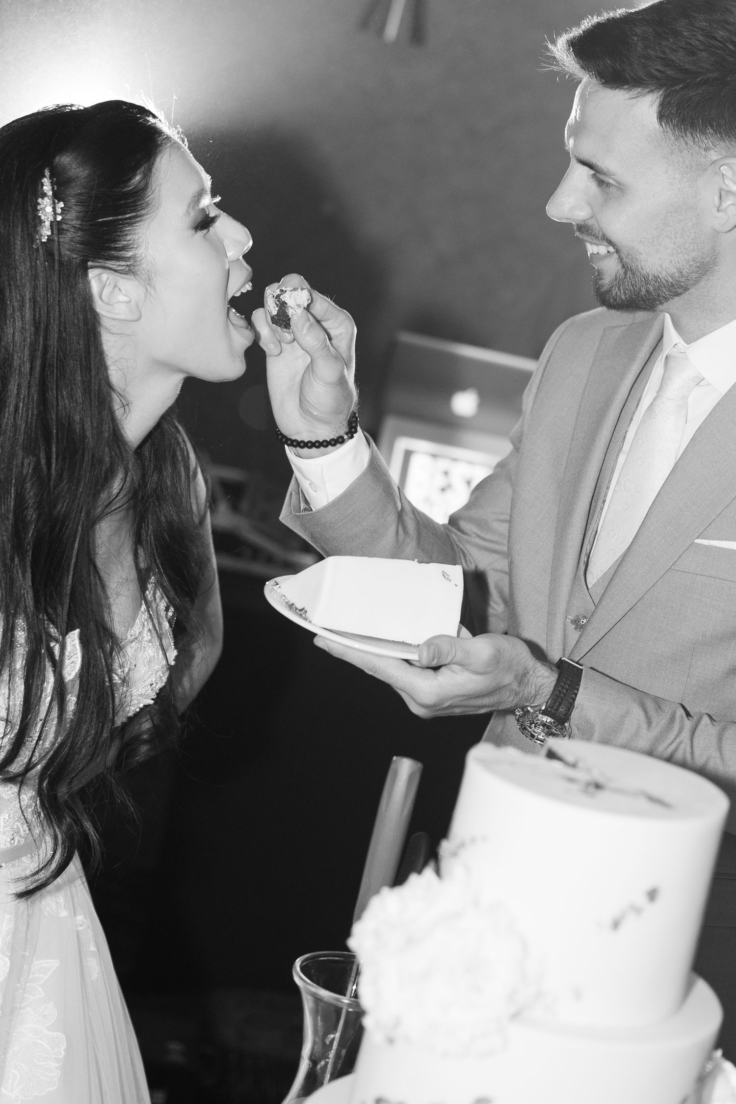 Black and white photo of groom feeding bride a piece of wedding cake at reception. Italy wedding photographer and filmmaker