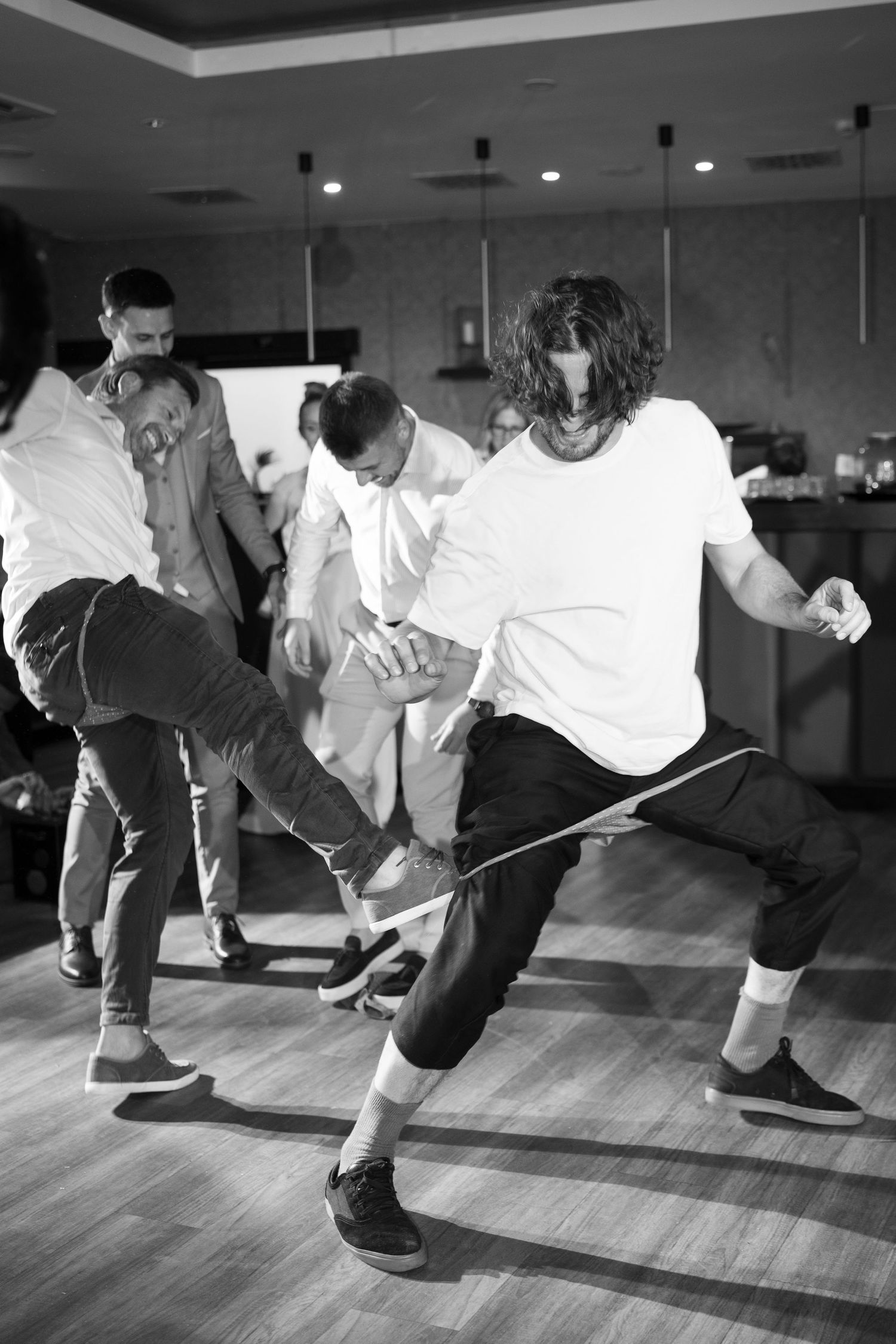 Men dancing energetically at a party in black and white photo. Italy wedding photographer and filmmaker