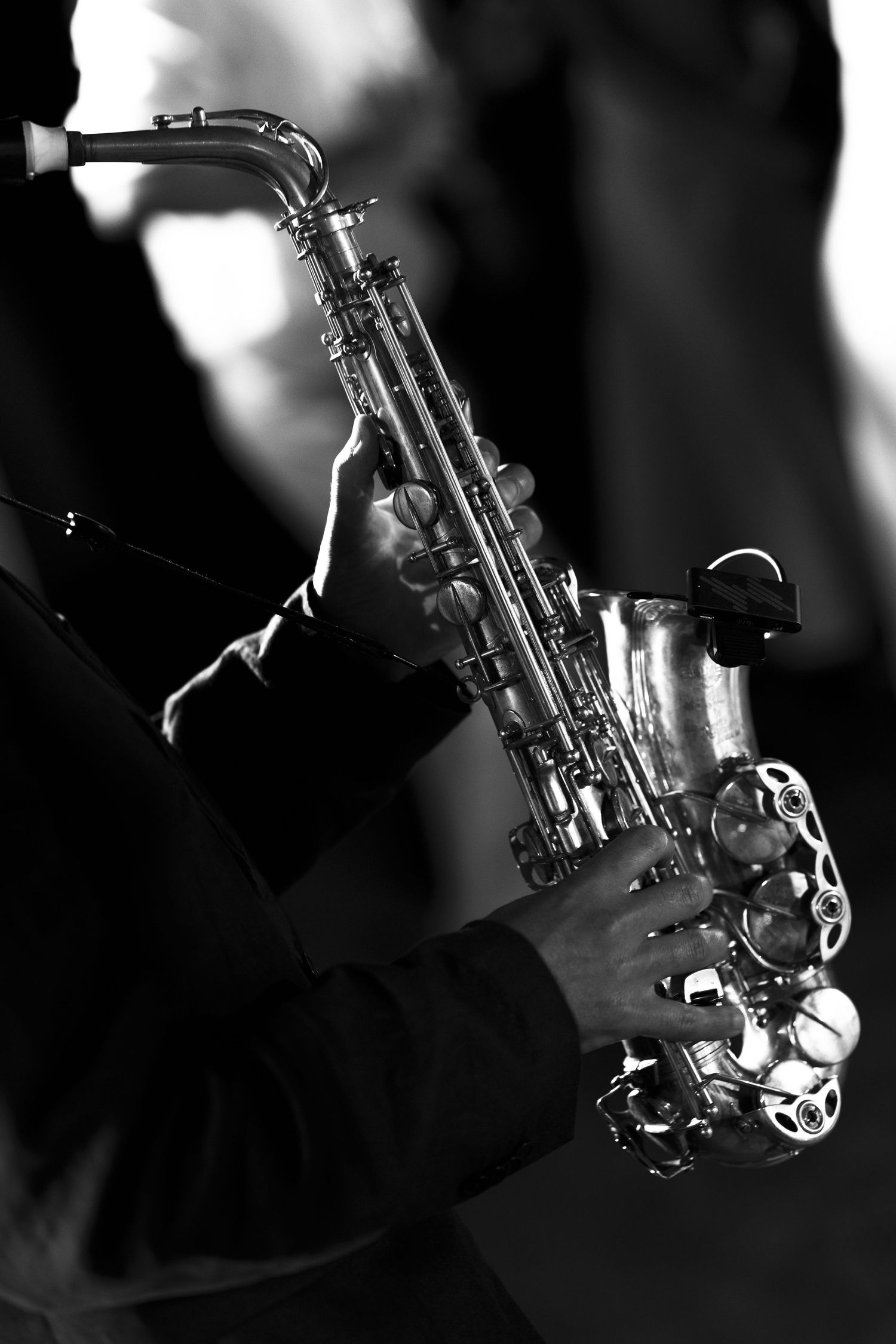 Black and white close-up of a musician's hands playing a silver alto saxophone with a microphone clipped to the bell.