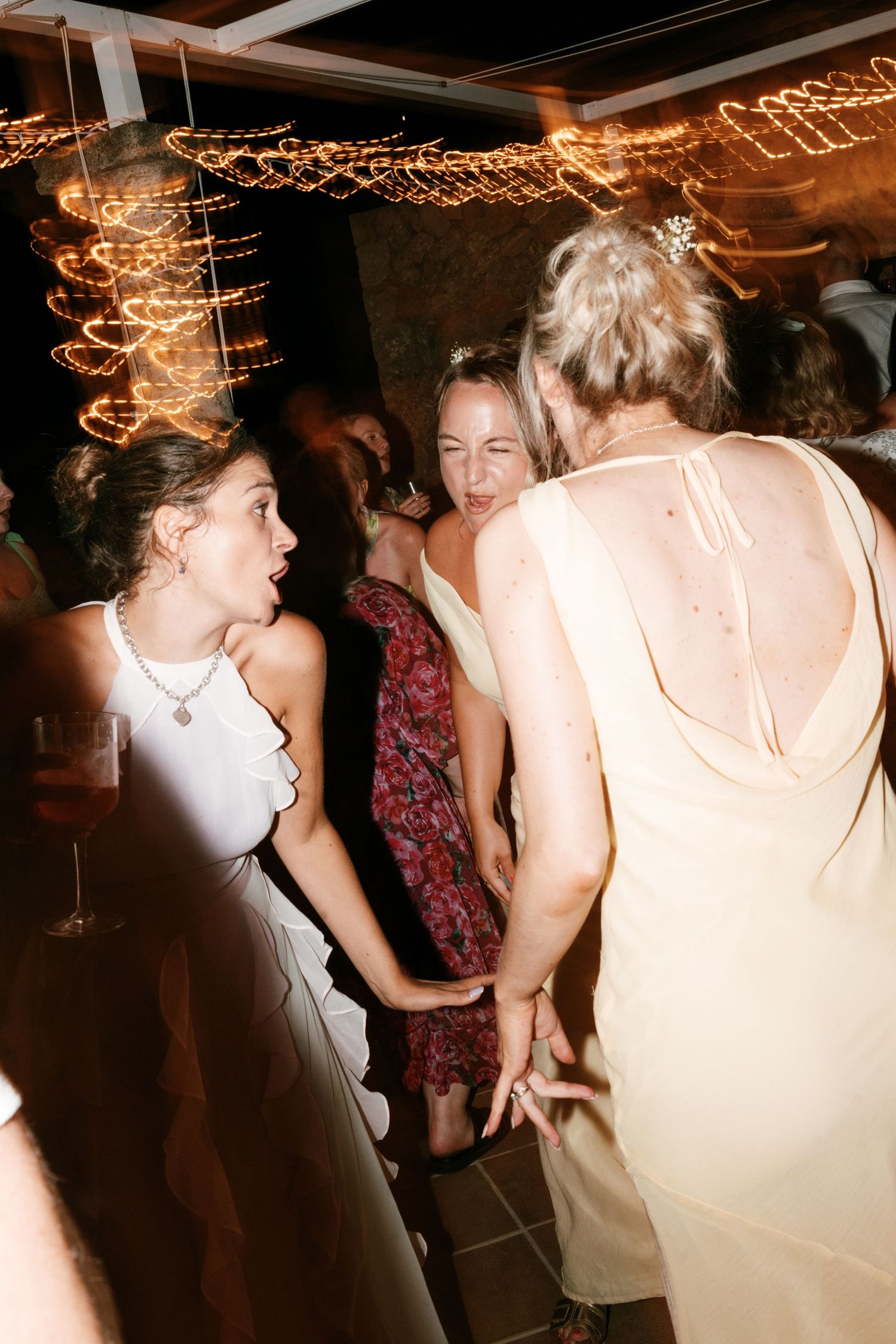 Wedding guests dancing and laughing together at lively evening reception with bokeh string lights. Tuscany wedding photographer, filmmaker