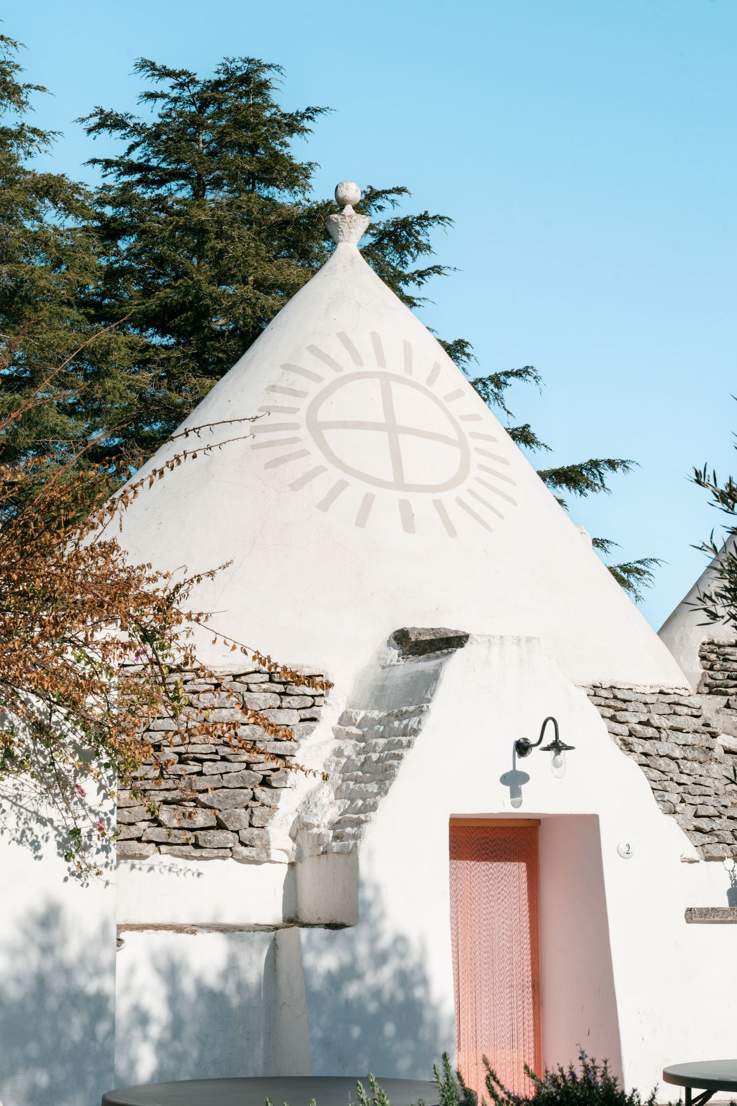 White trulli building with conical roof featuring painted sun symbol and pink door in Alberobello, Italy. Puglia wedding photographer,