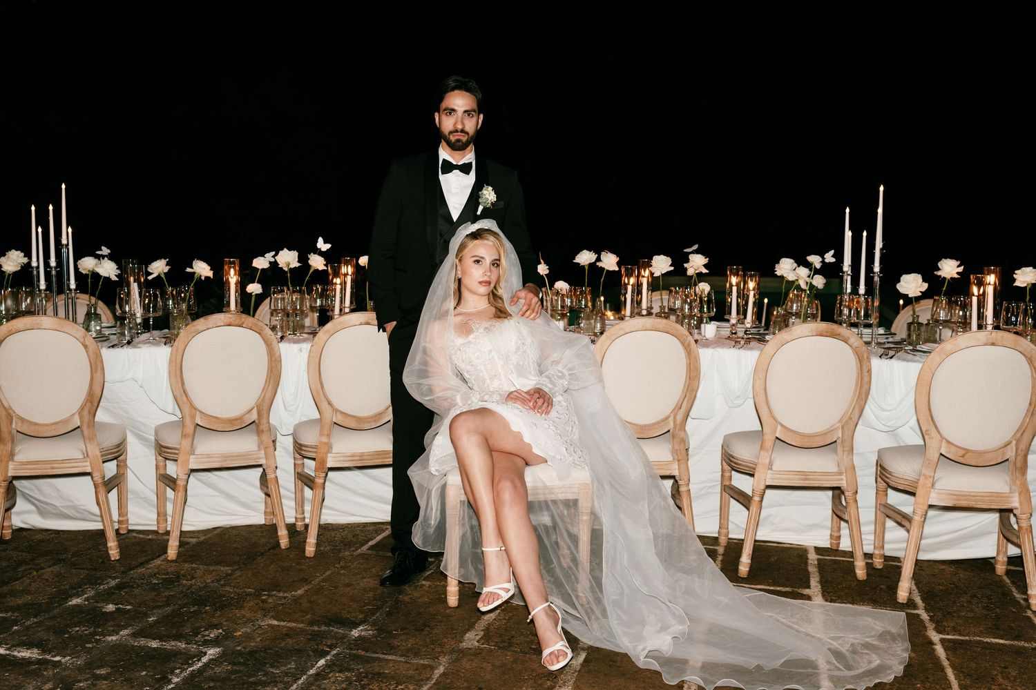 Bride and groom posing elegantly at a candlelit outdoor wedding reception table at night. Mallorca wedding photographer, filmmaker