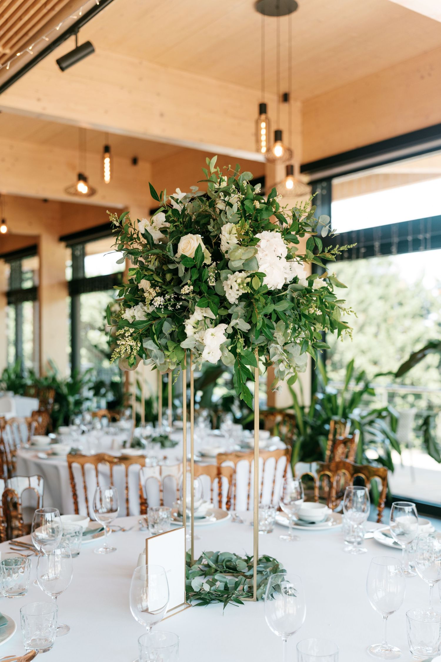 Tall gold floral centerpiece with white roses and greenery on wedding reception table. Italy wedding photographer and filmmaker
