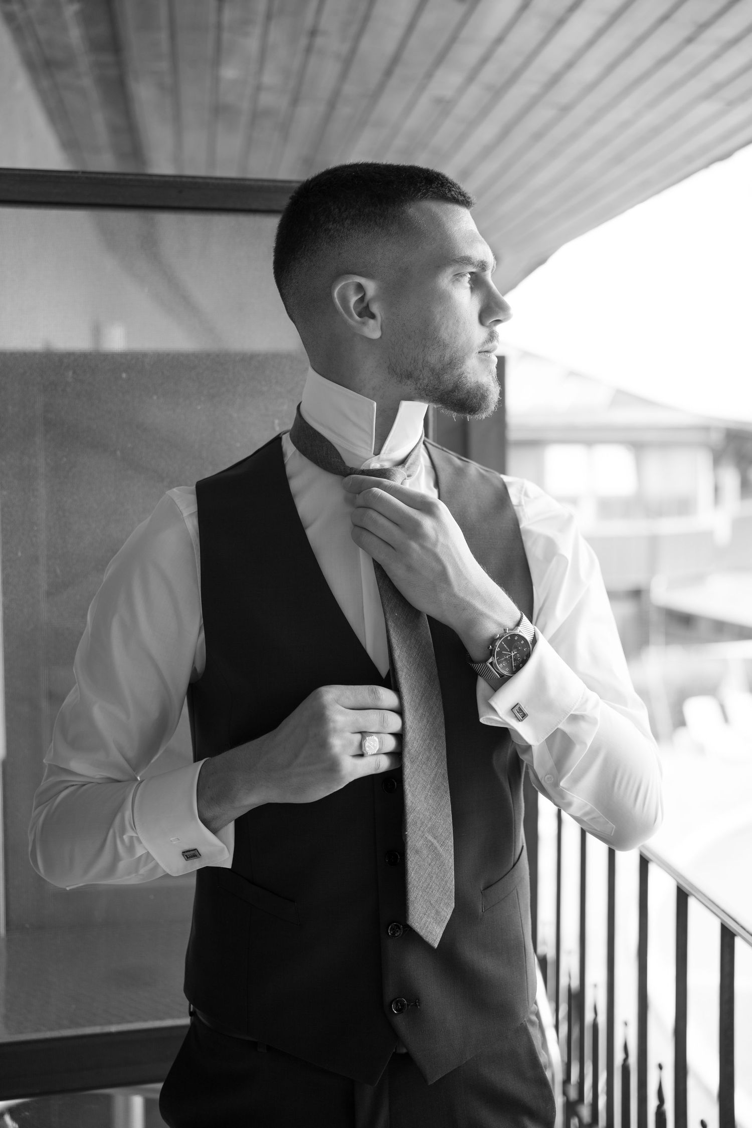 Black and white photo of groom in vest adjusting tie on balcony. Mallorca wedding photographer and filmmaker.