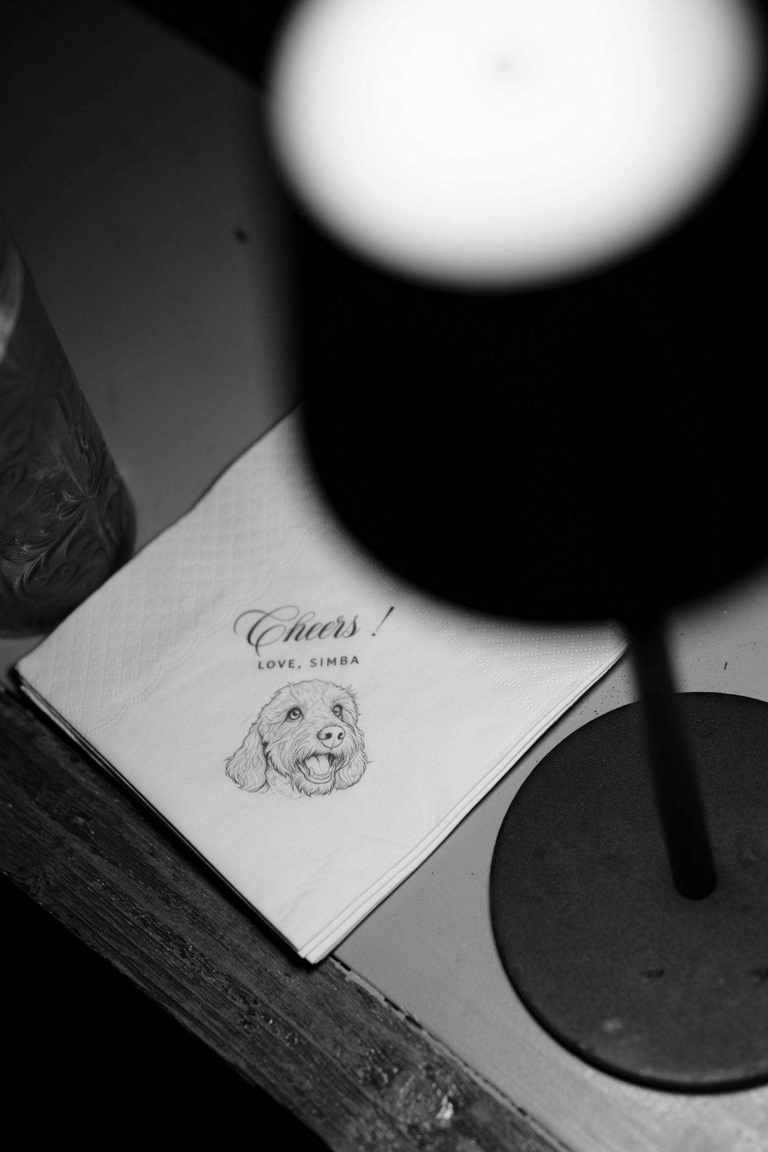 Black and white photo of a cocktail napkin with an illustrated dog and the text 