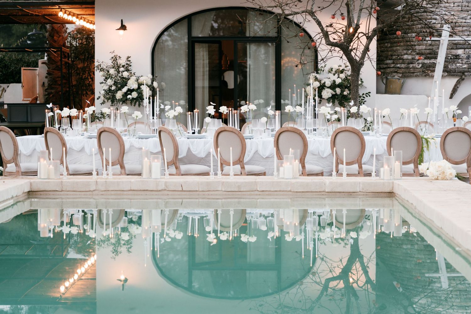 Elegant outdoor wedding reception table reflected in a turquoise pool beside a white arched building. Mallorca wedding photographer, film
