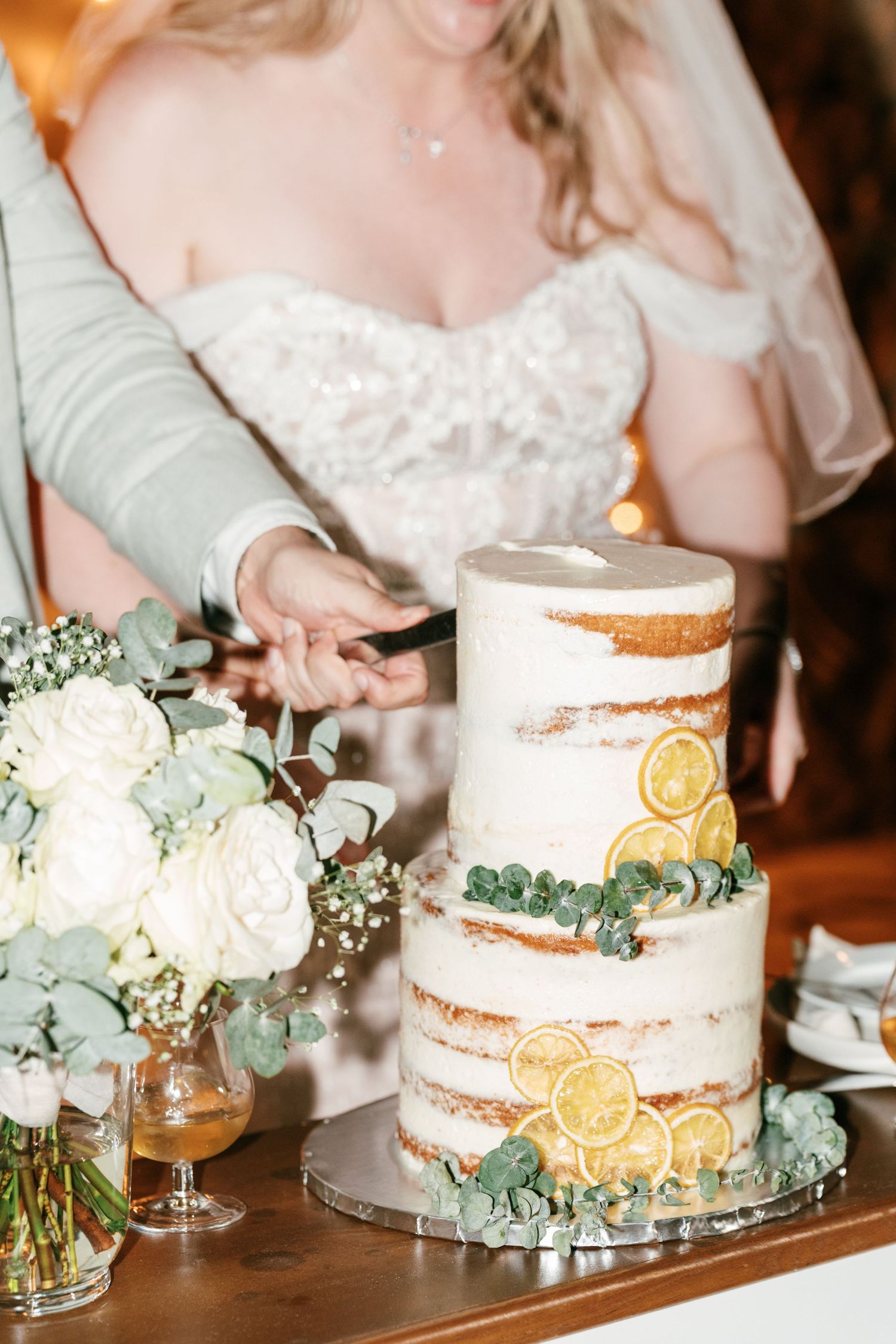 Bride and groom cut a two-tier naked wedding cake decorated with lemon slices and eucalyptus. Tuscany wedding photographer, filmmaker