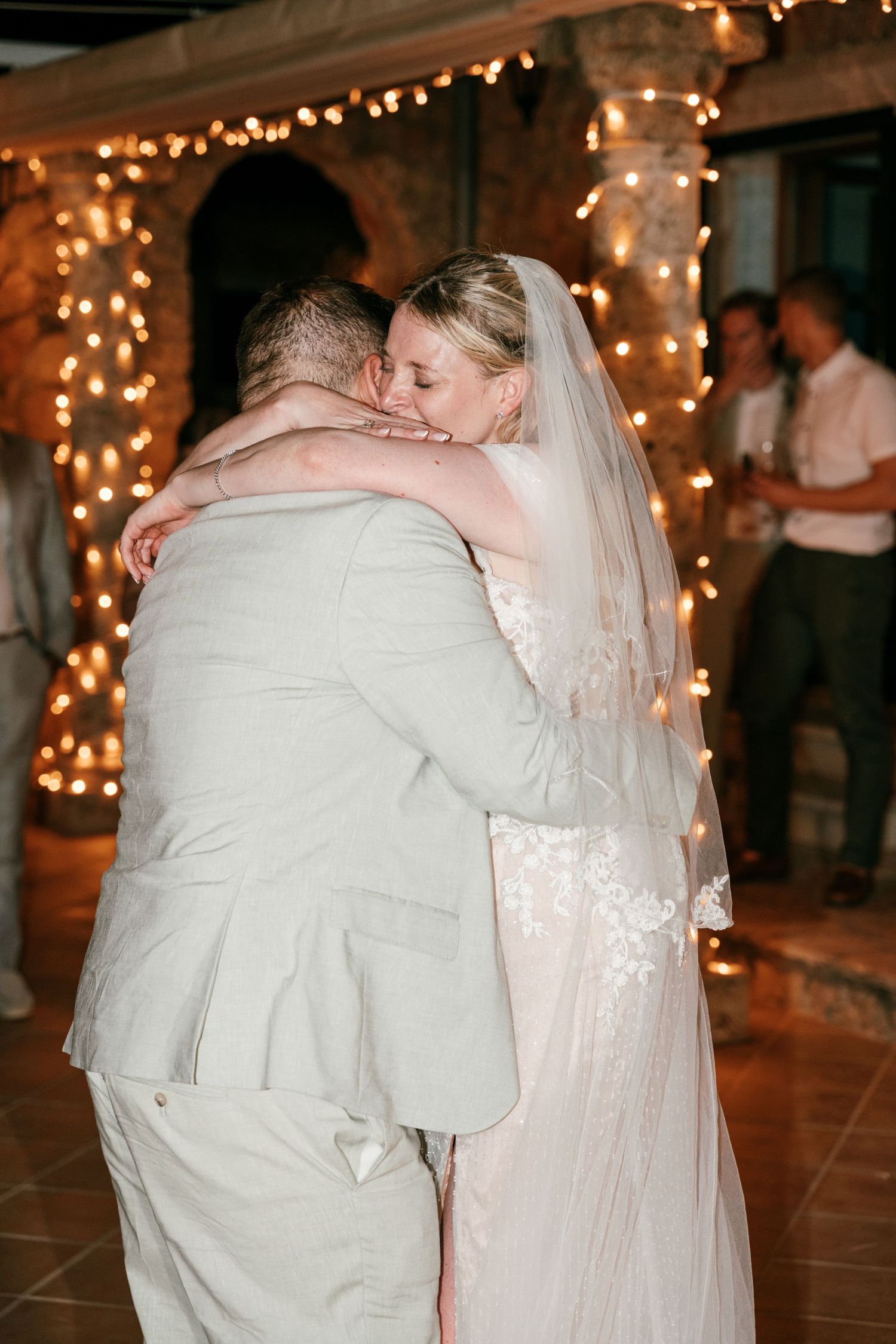 Bride and groom share emotional first dance embrace, surrounded by warm fairy lights at wedding reception. Tuscany wedding photographer, fil