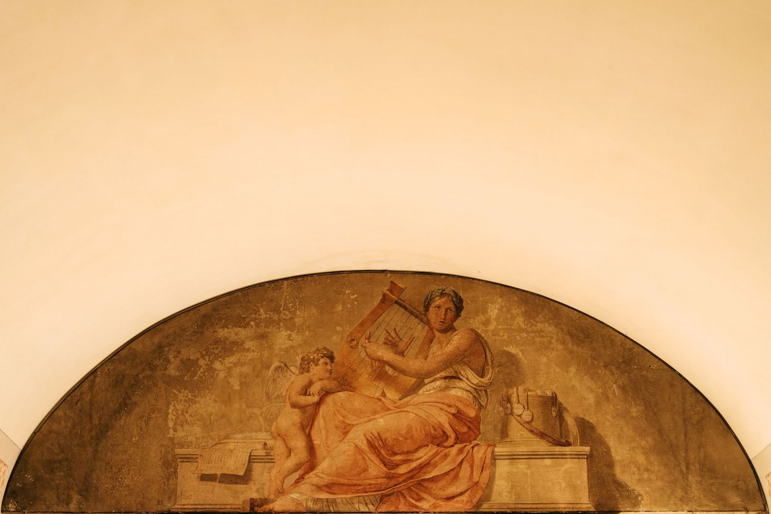 Classical lunette fresco of a seated robed woman playing a lyre beside a winged cherub, painted in warm earth tones on an arched wall.