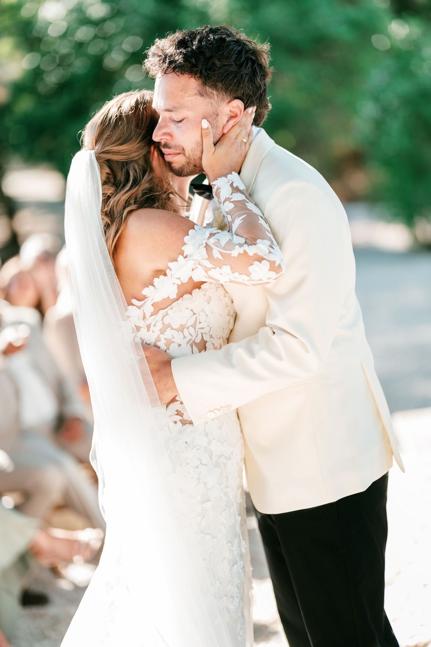 Bride and groom share their first kiss at outdoor wedding ceremony, bride in lace gown with veil.
