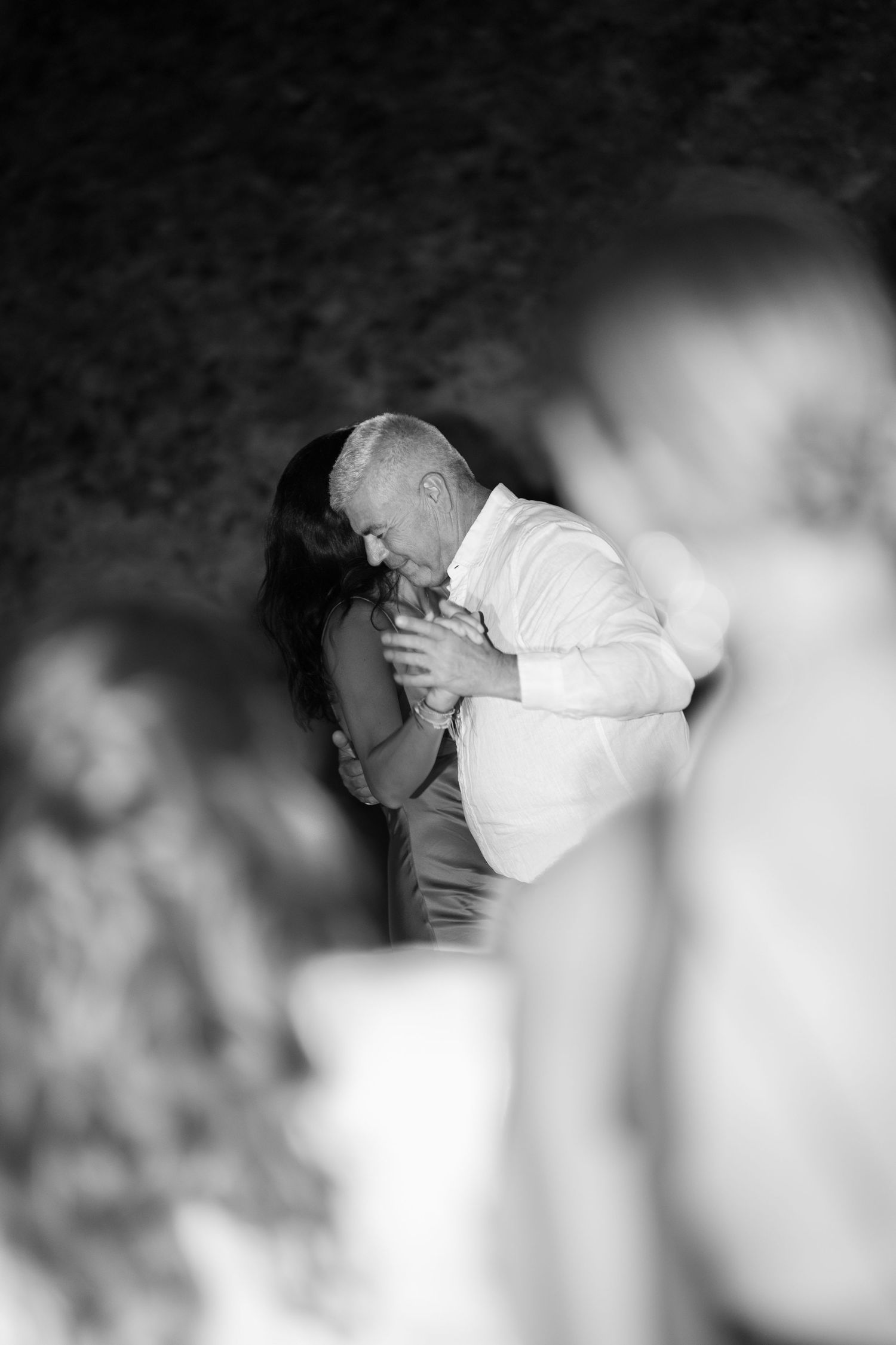 Black and white photo of a man in white shirt kissing a woman's hand at a wedding reception.