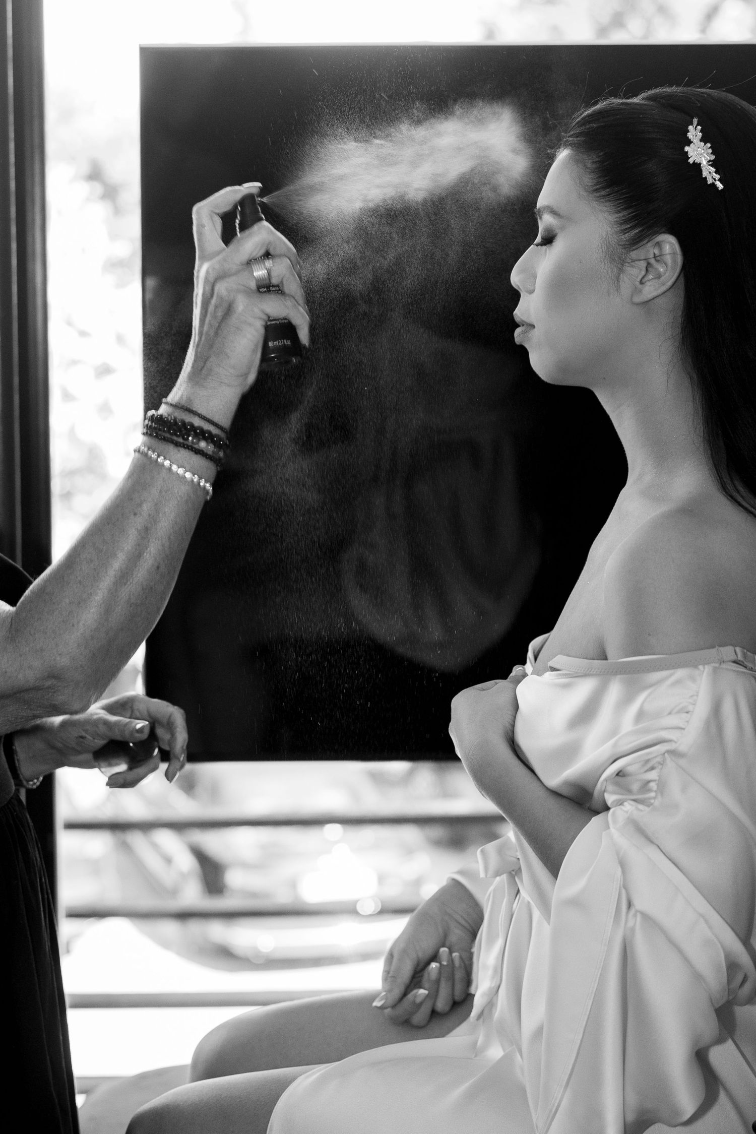 Black and white photo of a makeup artist setting a brides face with setting spray before her wedding. Italy wedding photographer and filmmak